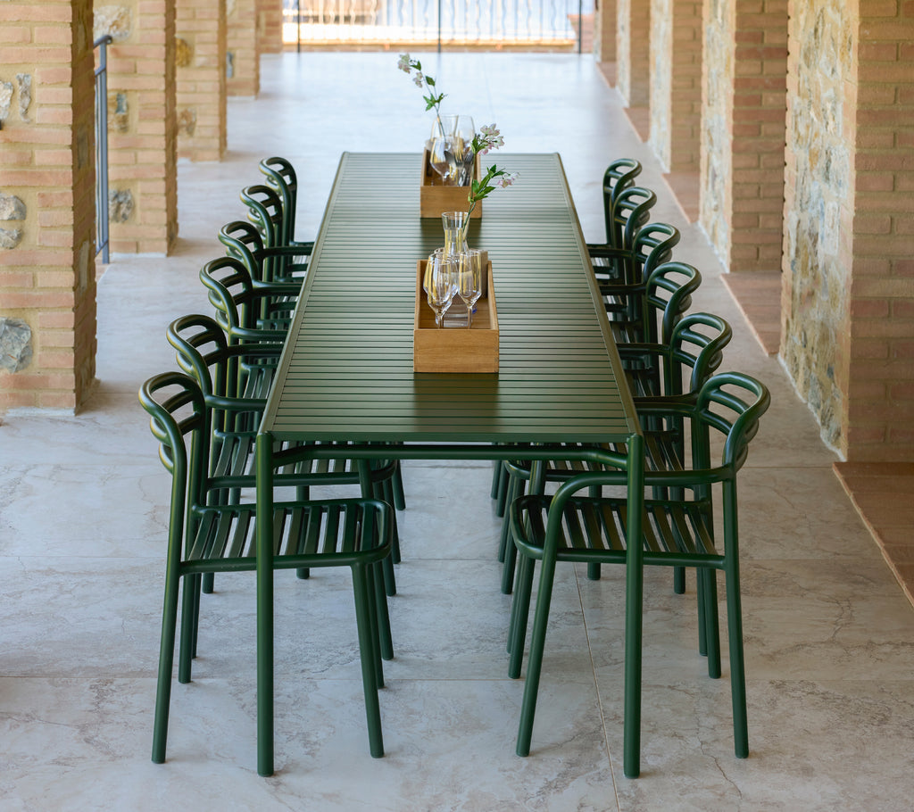 Bliss chairs with armrests in dark green arranged around a long extendable table featuring a central decorative tray with flowers.