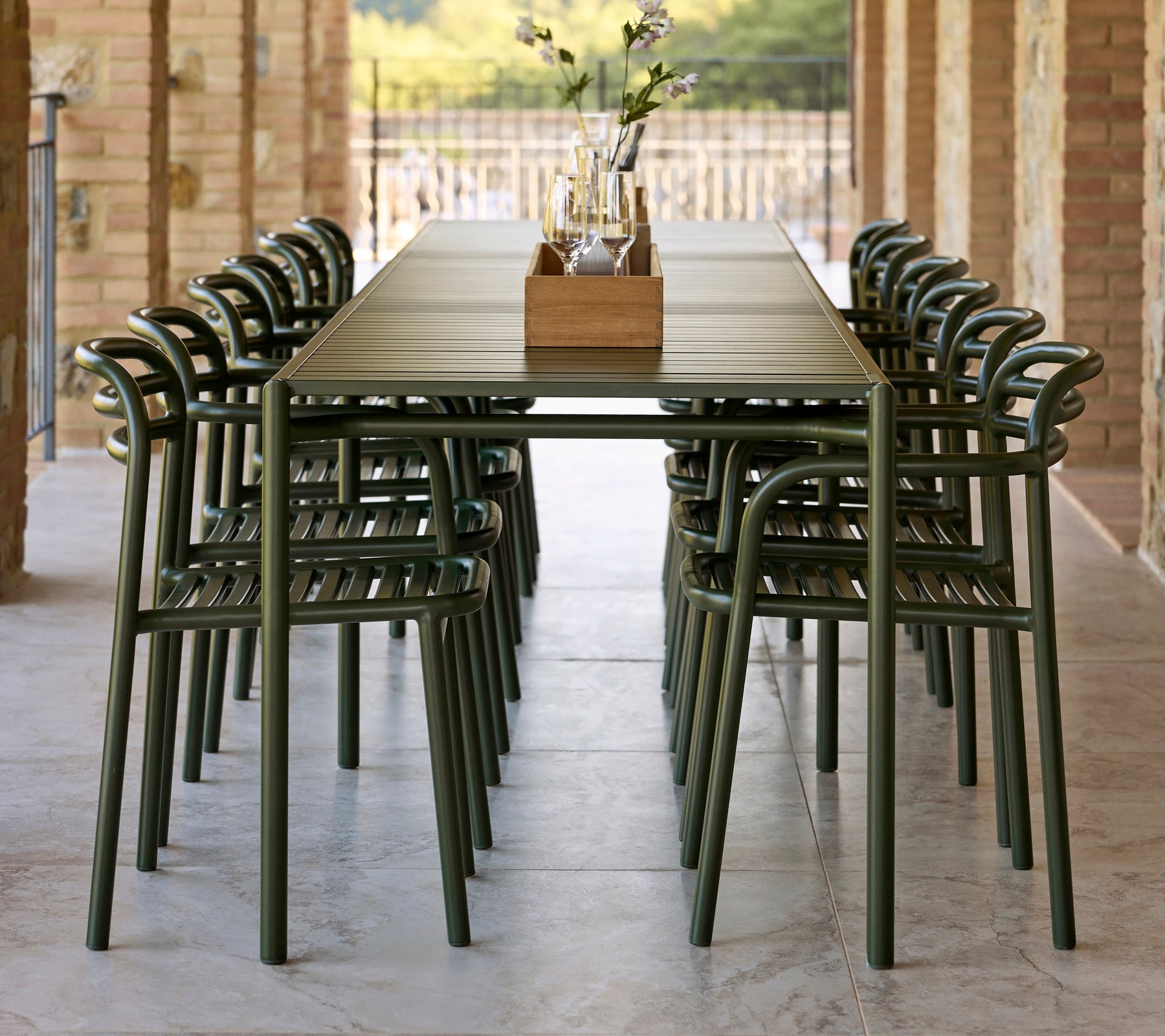Een lange tafel gedekt met donkergroene Bliss-stoelen met armleuningen, aangevuld met een decoratief middelpunt.
