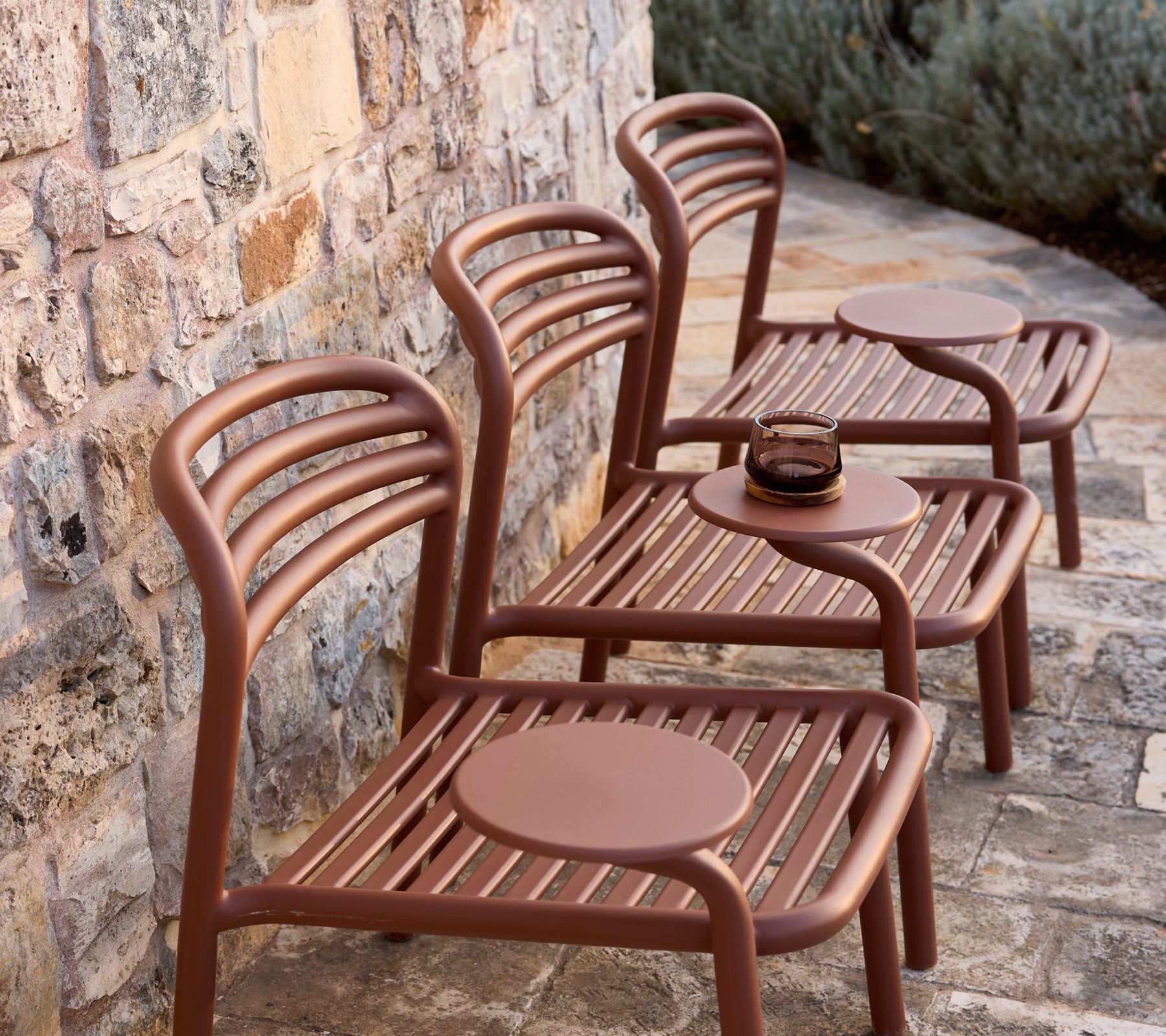 Drie moderne bruine stoelen met ronde tafels tegen een stenen muur.