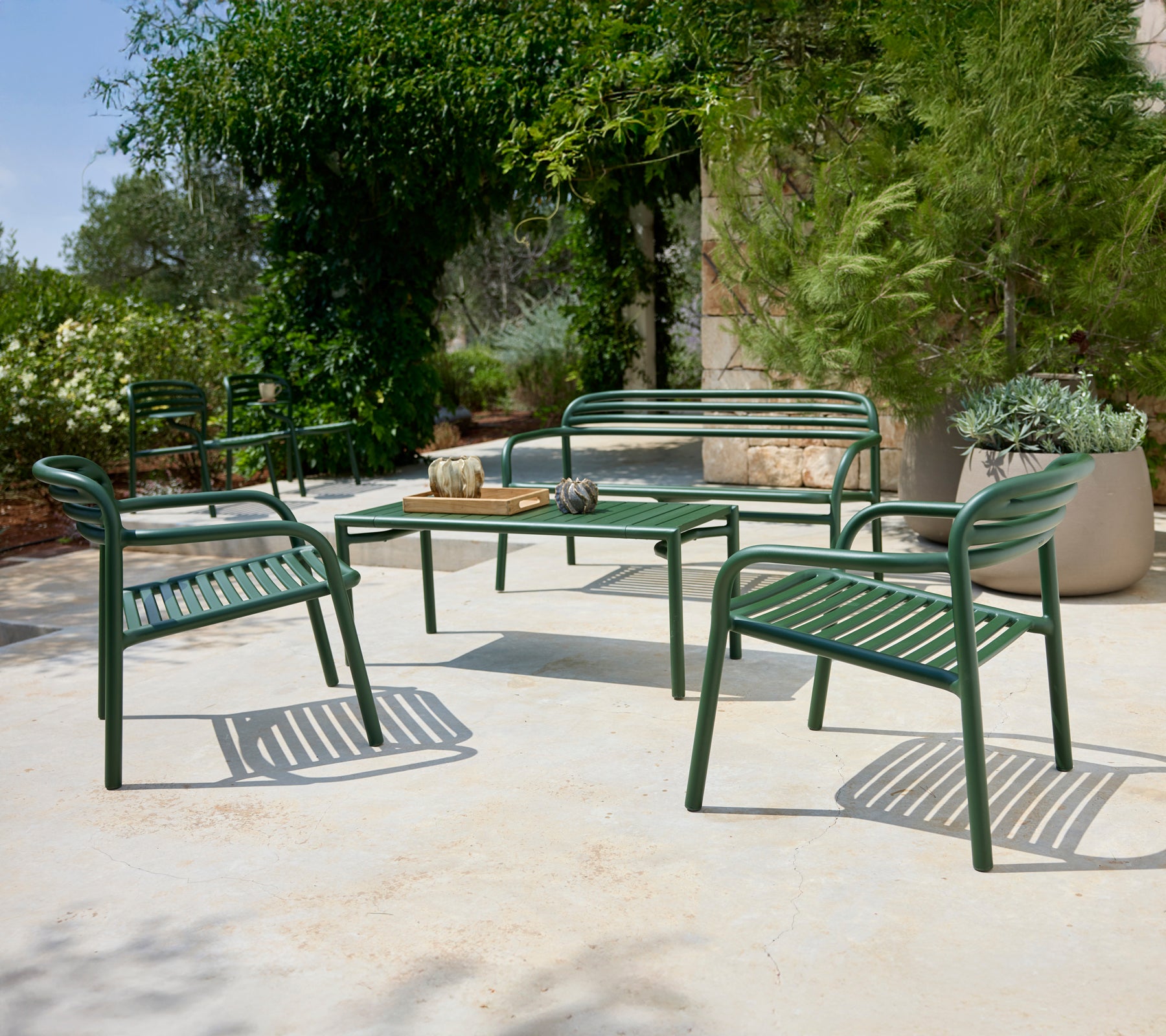 Groene buitensitgelegenheid met stoelen en bank rond een tafel.
