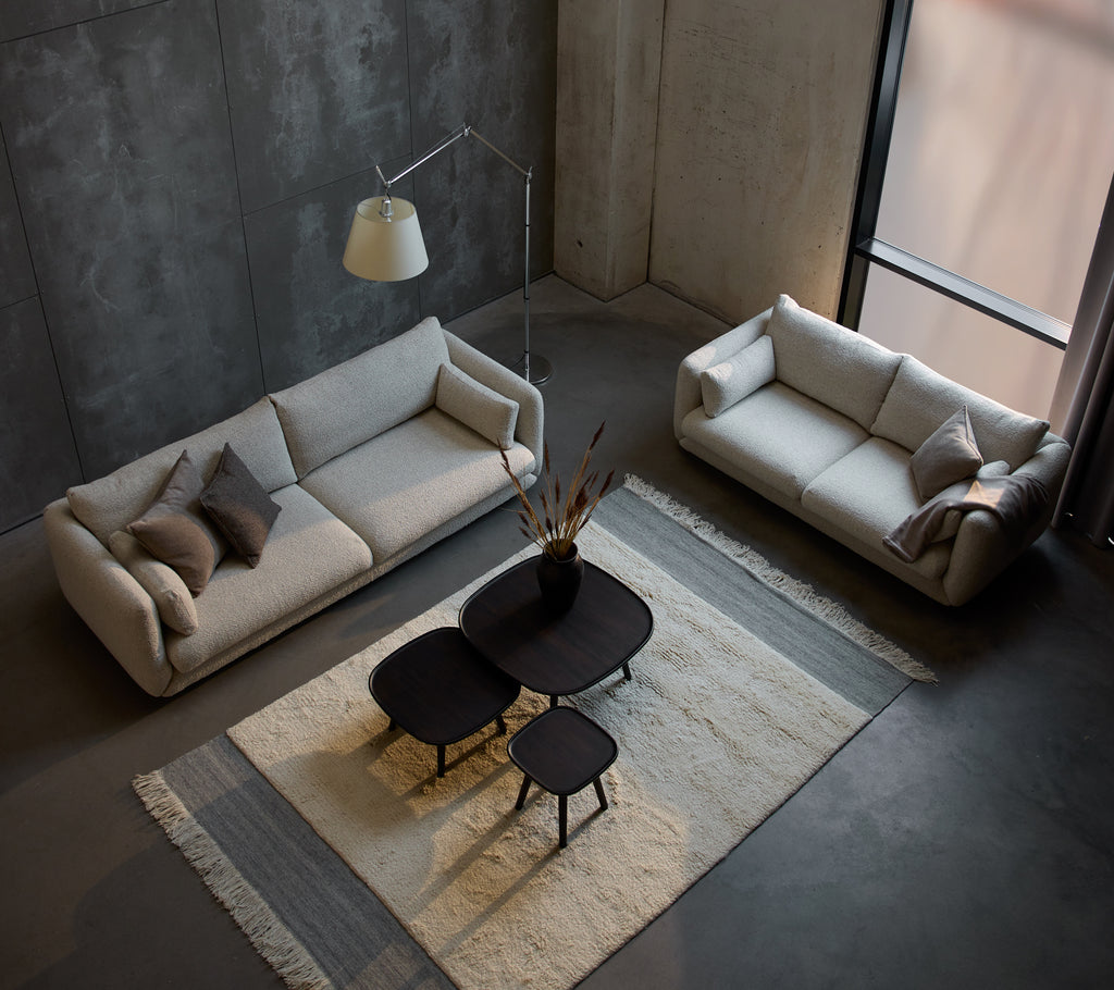 Een moderne zithoek met een Bloom 3-zitsbank, een kleinere 3-zitsbank en stijlvolle Pace salontafels op een gestructureerd tapijt.