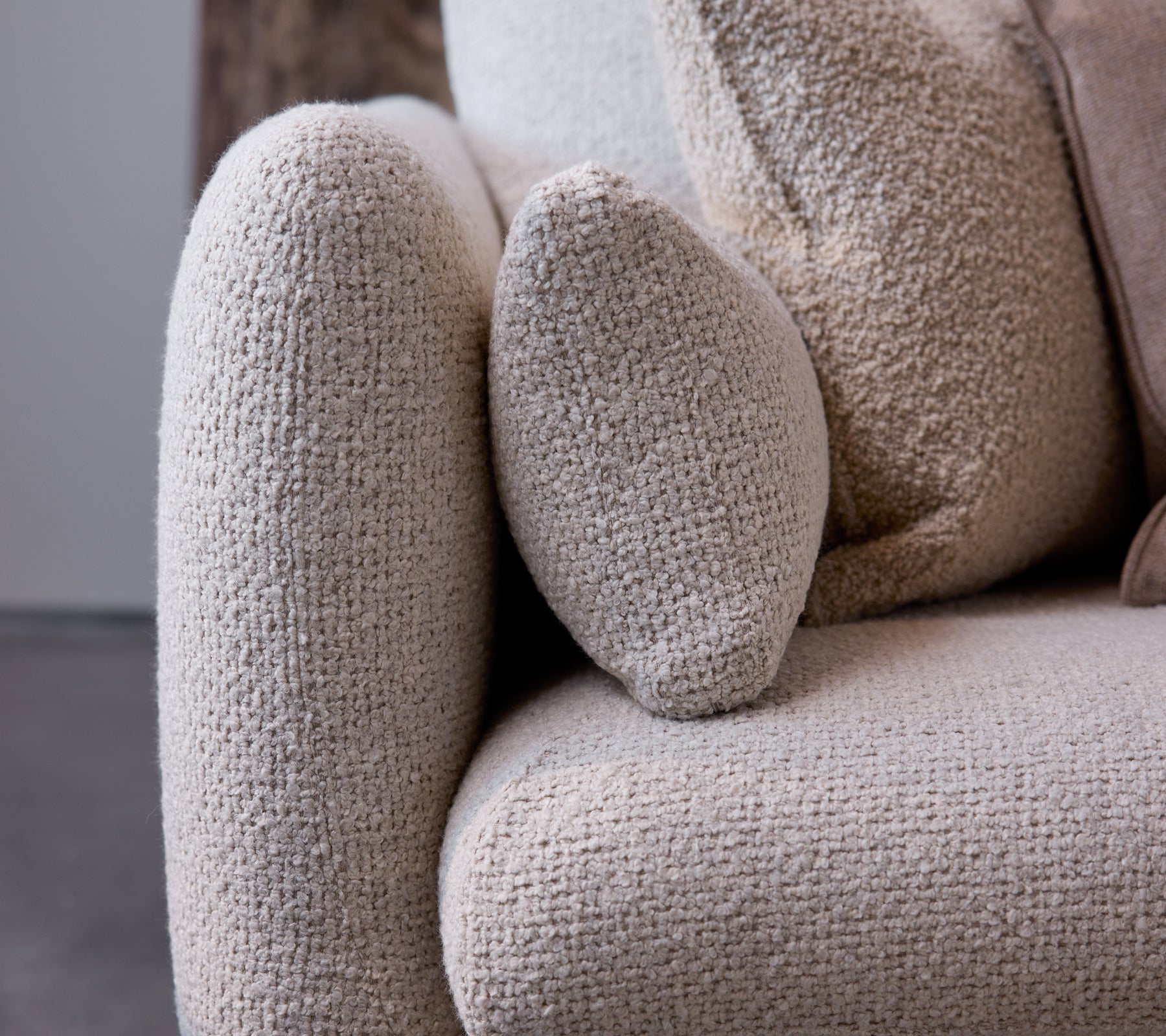 Close-up van de armleuning van een Bloom-sofa in een zandflairtextuur, die een rond ontwerp en zachte, comfortabele stof laat zien.