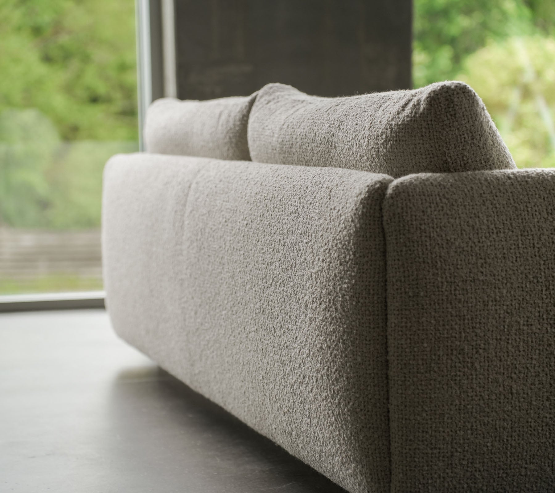 Moderne bank met een gestructureerde zandkleurige stof, benadrukt door elegante teakpoten, die de flair van Cane-line en zachte kussens toont.