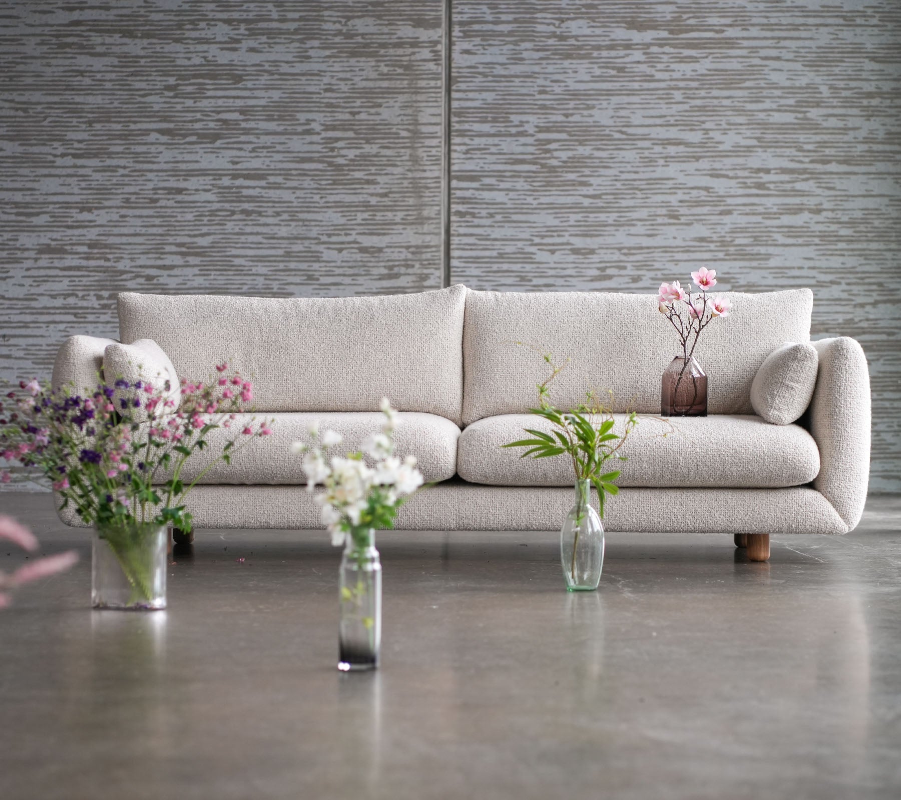 Een lichtkleurige bank met teak poten, omringd door vazen met bloemen, die een mengsel van elegantie en Cane-line flair tentoonstelt.