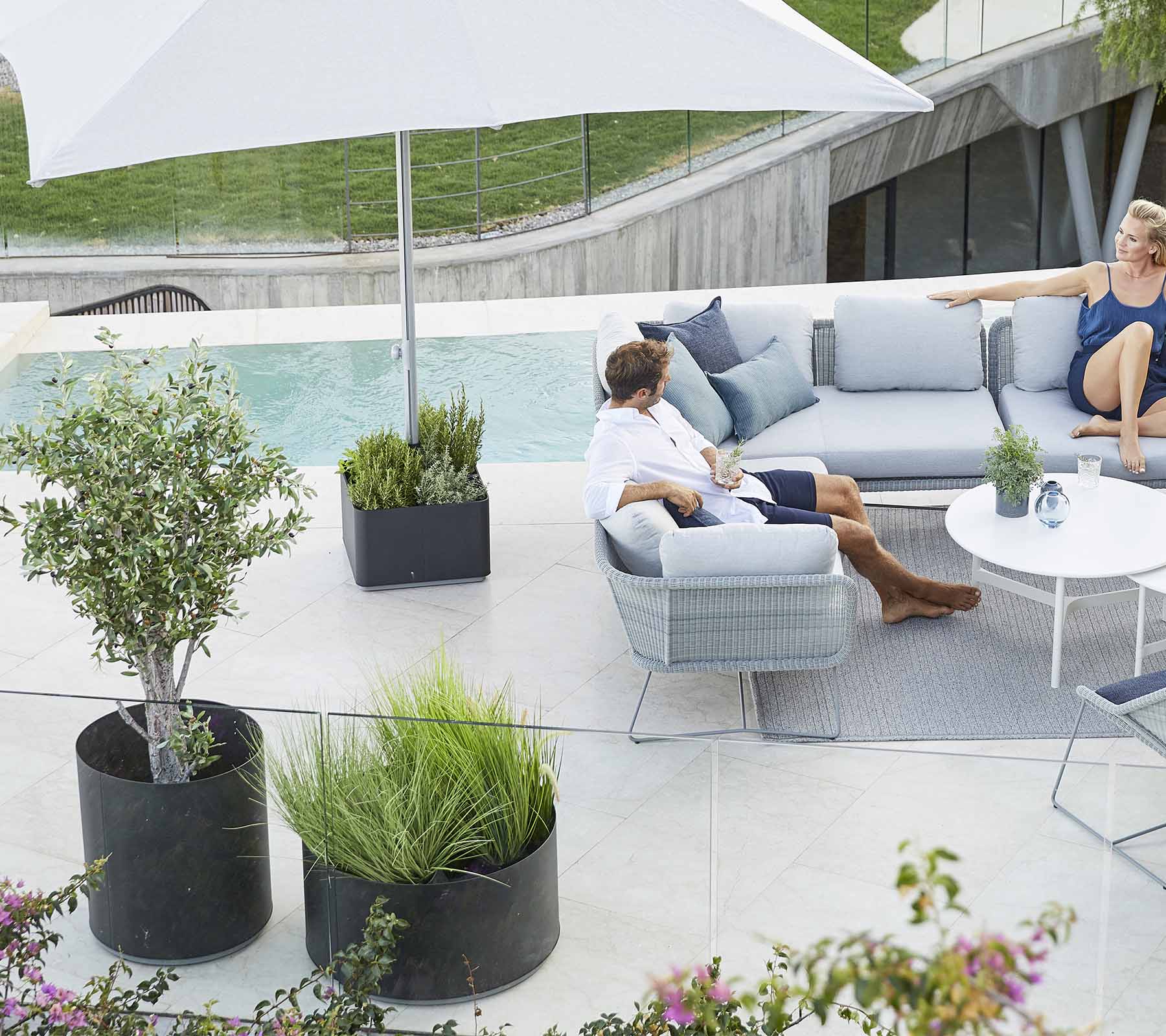 Een stijlvolle buitenzitruimte met een comfortabele sofa, planten en een grote parasol, perfect om te ontspannen.