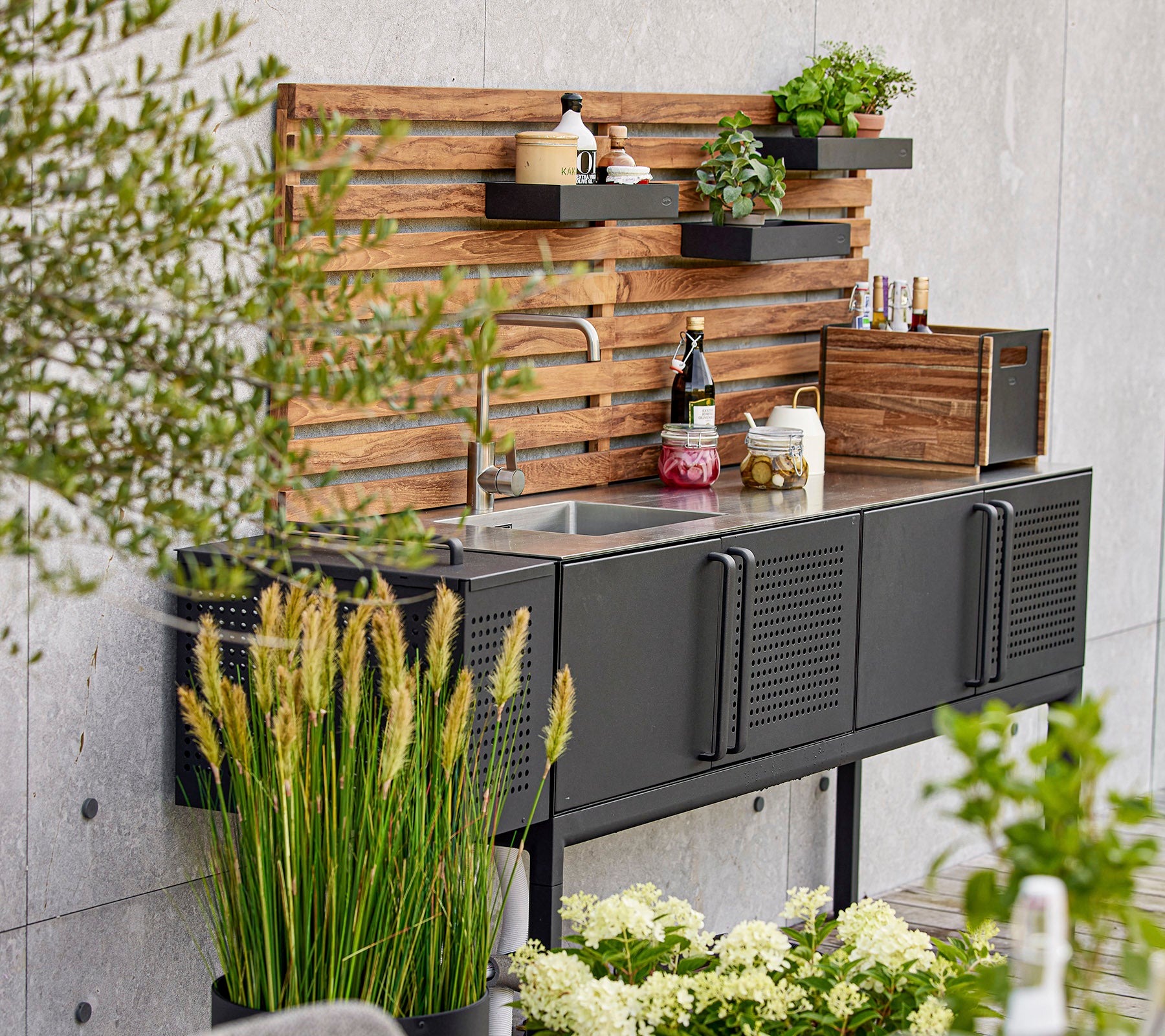 Moderne zwarte keukeneenheid met een gootsteen, houten planken en verschillende planten, wat een stijlvolle en functionele werkruimte creëert.