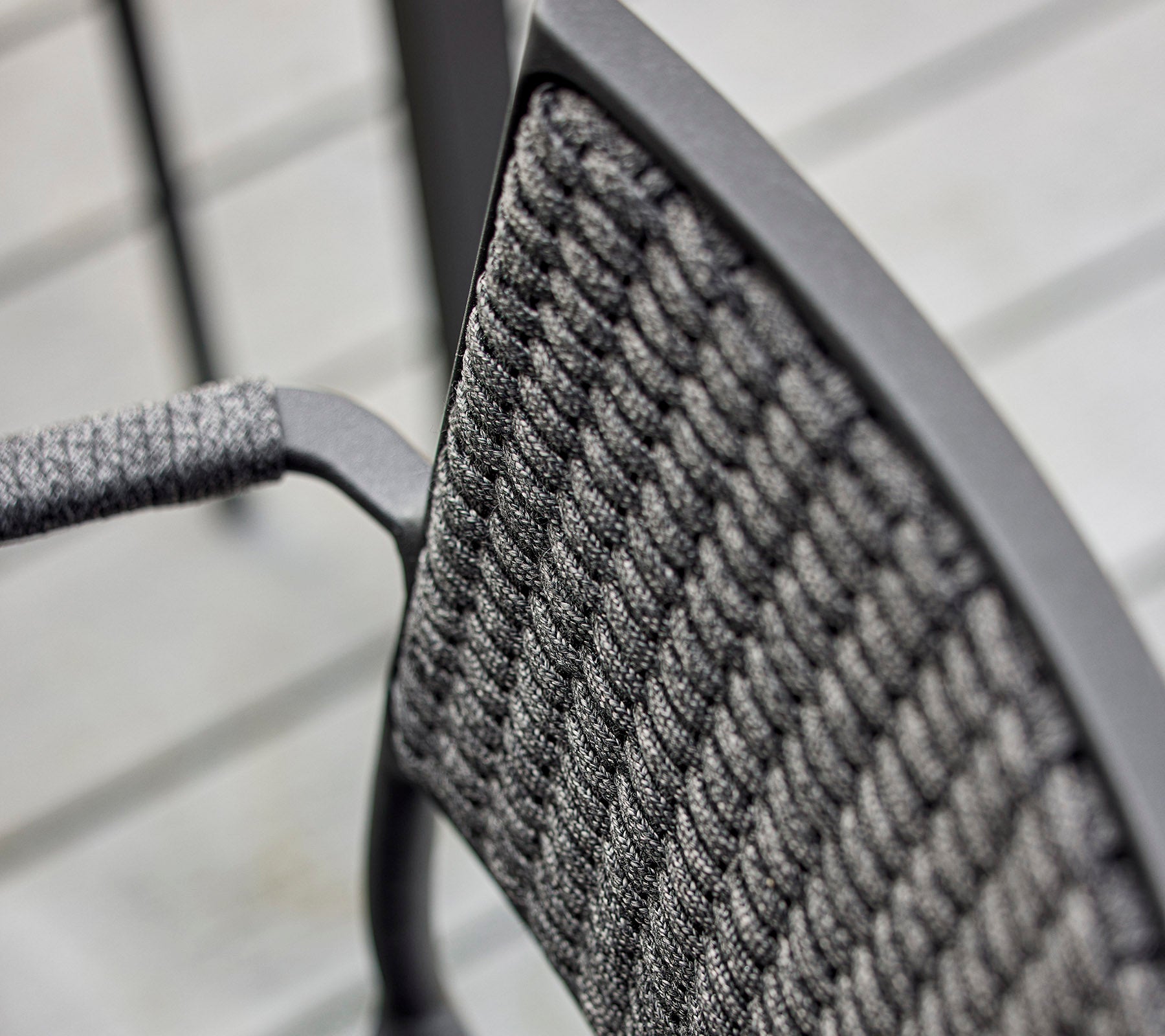 Close-up van de rugleuning van een stoel met een gestructureerd geweven ontwerp en een slank metalen frame, dat modern vakmanschap benadrukt.