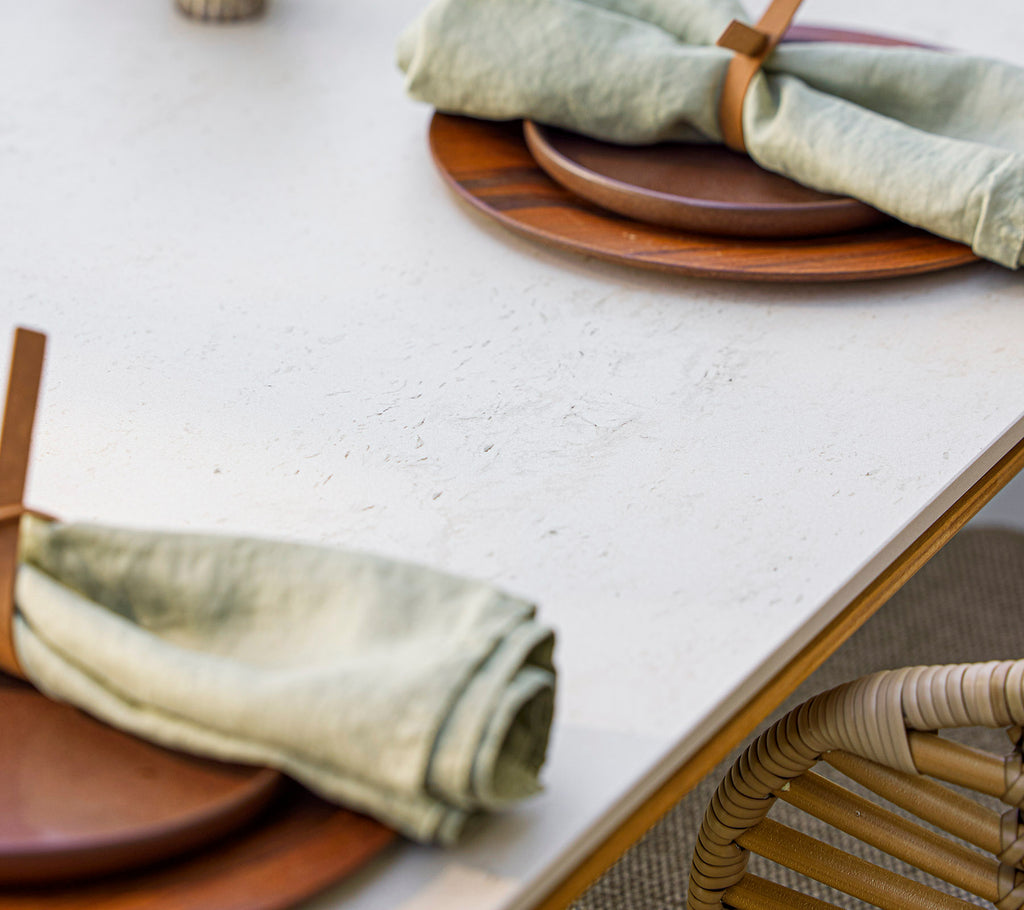 Tafeldekking met houten borden en elegant opgerolde groene servetten vastgezet met een houten houder, die een natuurlijke en uitnodigende sfeer creëert.