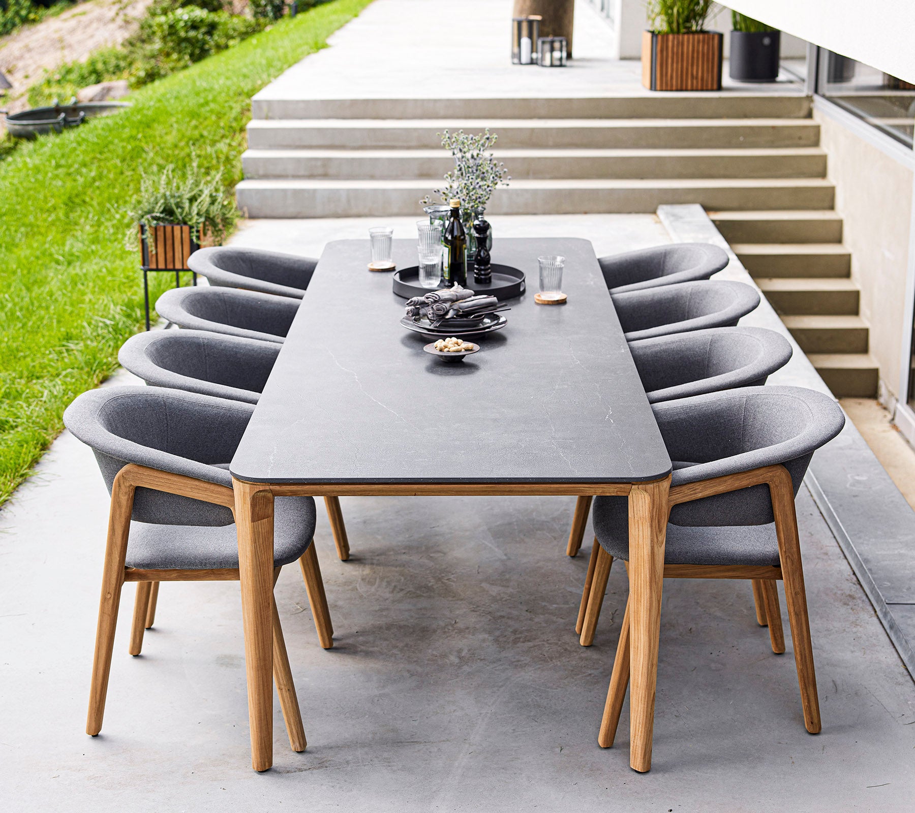 Een moderne eettafel met acht grijze stoelen, met decoratieve items en planten op de tafel, geplaatst in een elegante buitenruimte.