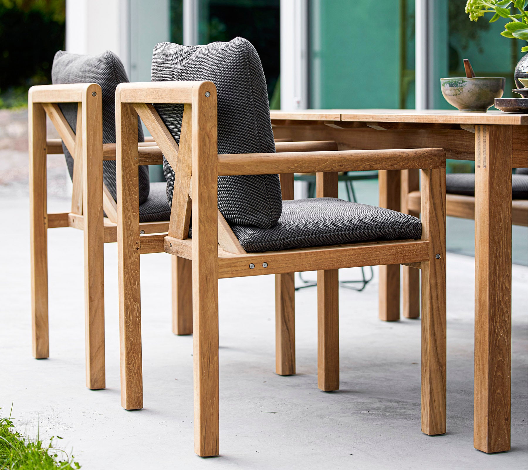 Houten stoelen met grijs gevoerde zittingen, ontworpen voor comfort, complementeren een houten tafel in een stijlvolle omgeving.