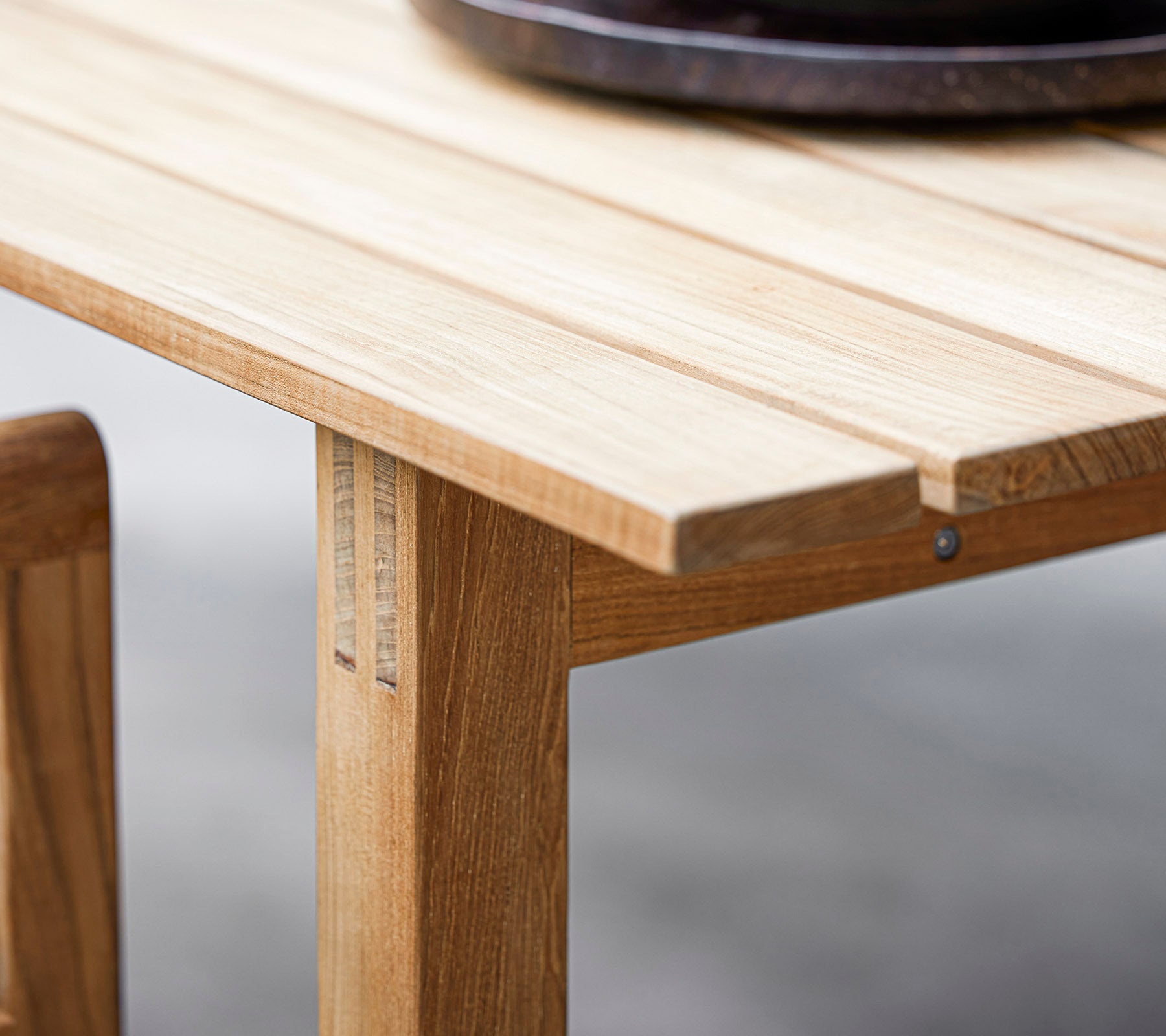 Close-up van een houten tafel met lamellenontwerp en een donkere ronde decoratieve schaal bovenop. Perfect voor moderne eetesthetiek.