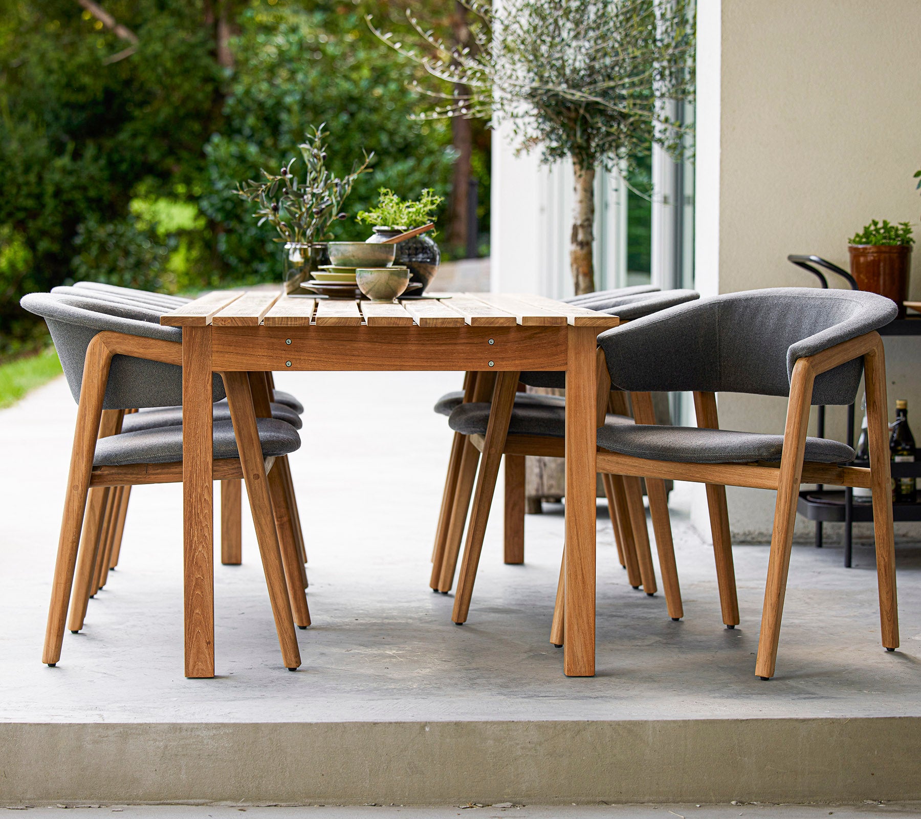 Een stijlvolle houten eettafel omringd door vier grijze, gevoerde stoelen, perfect voor buitenbijeenkomsten.