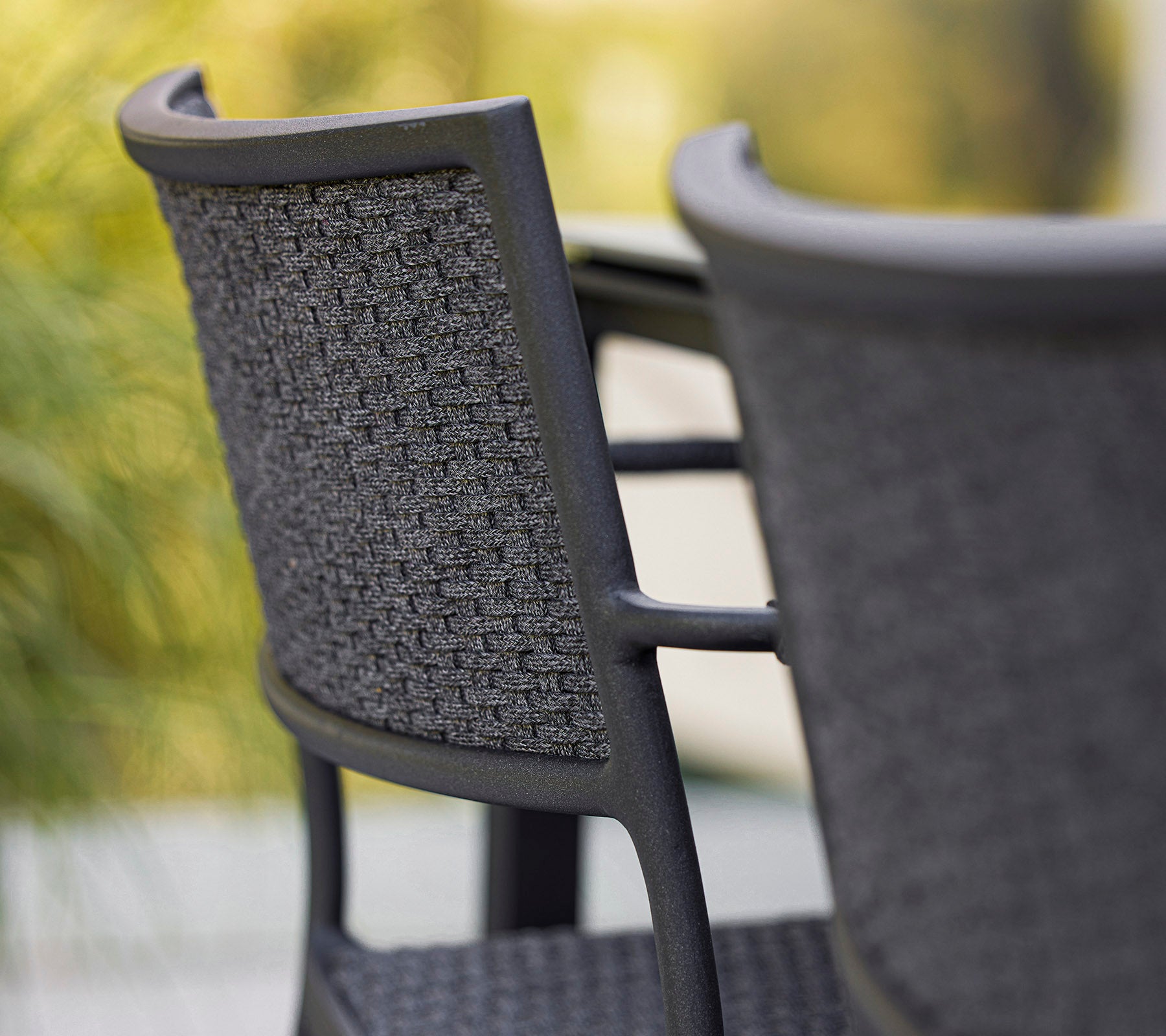 Close-up van een stijlvolle stoel met een gevlochten rugleuning, die een modern ontwerp in grijstinten laat zien. Perfect voor hedendaagse ruimtes.