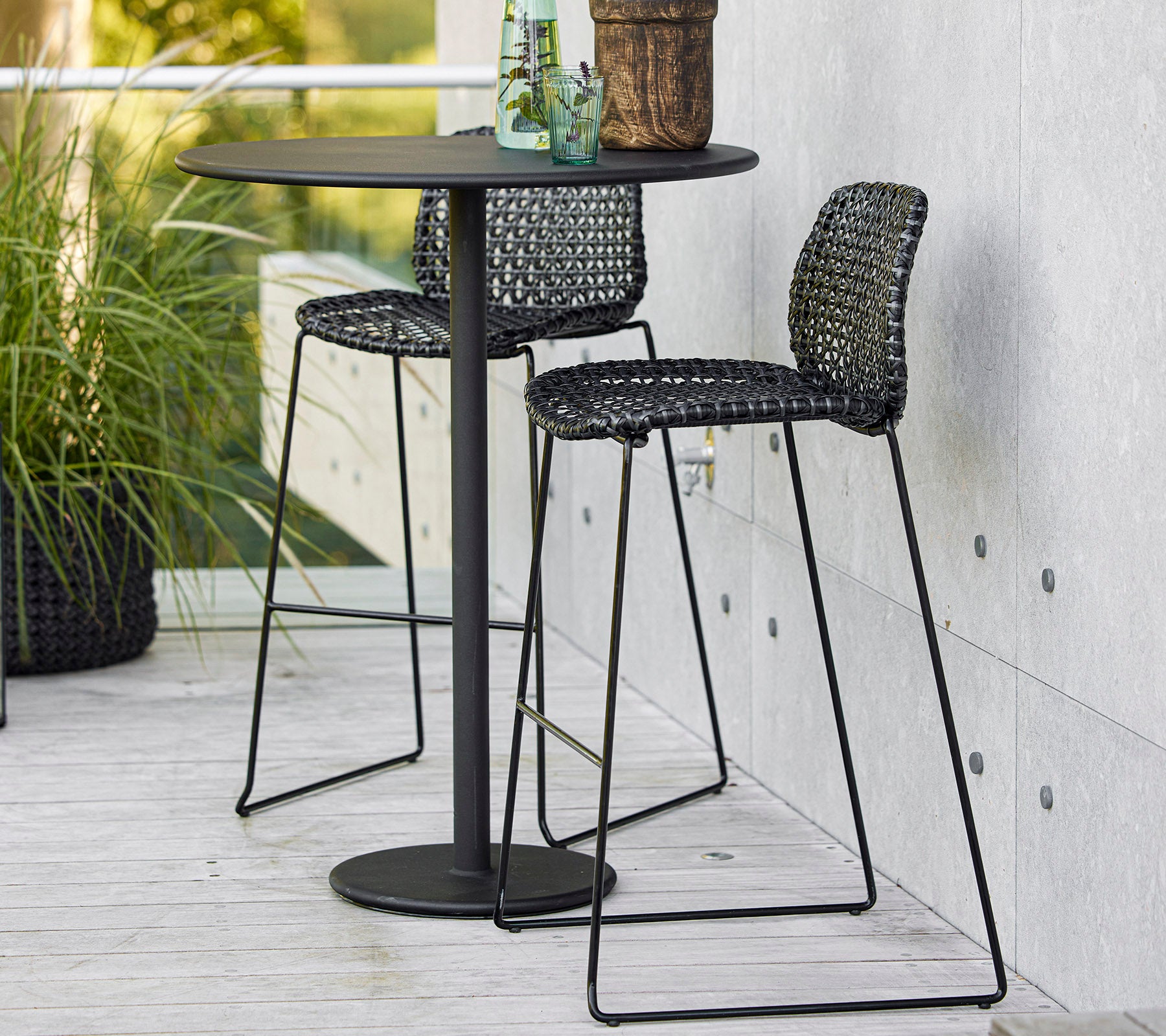 Stijlvolle zwarte bartafel met twee gevlochten stoelen en een potplant, perfect voor casual dining of ontspanning.