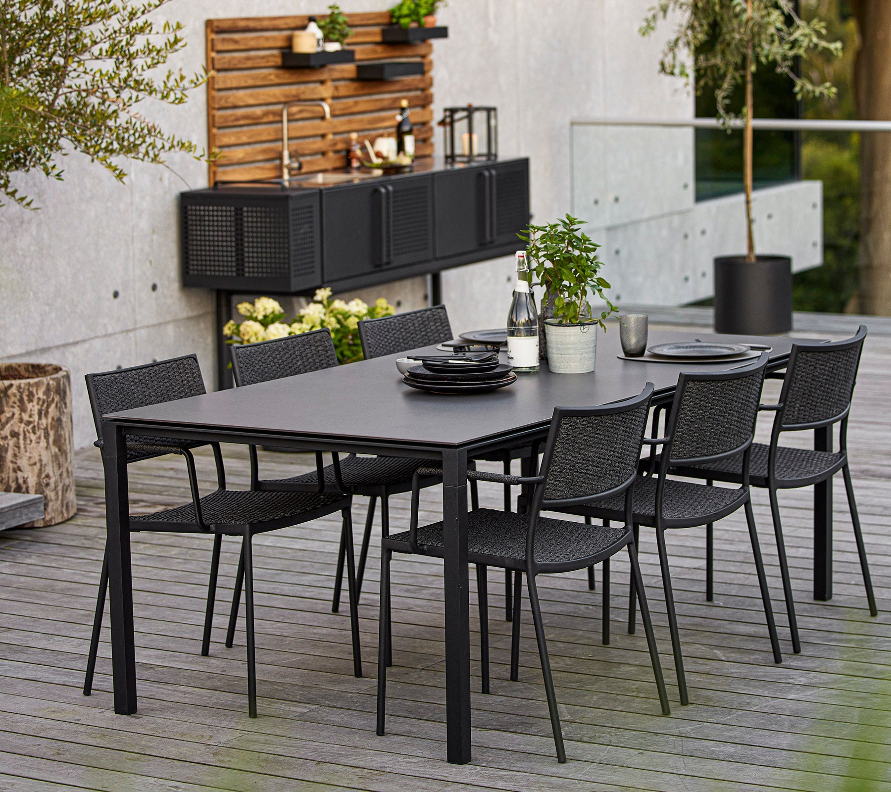 Een moderne eetkamer set met een grote rechthoekige tafel en zes zwarte gevlochten stoelen, benadrukt door decoratieve elementen en groen.