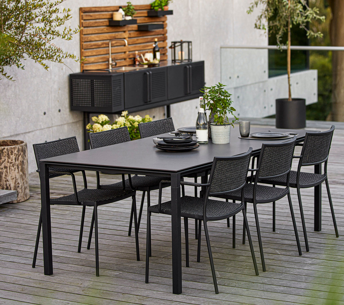 Een moderne eetkamer set met een grote rechthoekige tafel en zes zwarte gevlochten stoelen, benadrukt door decoratieve elementen en groen.