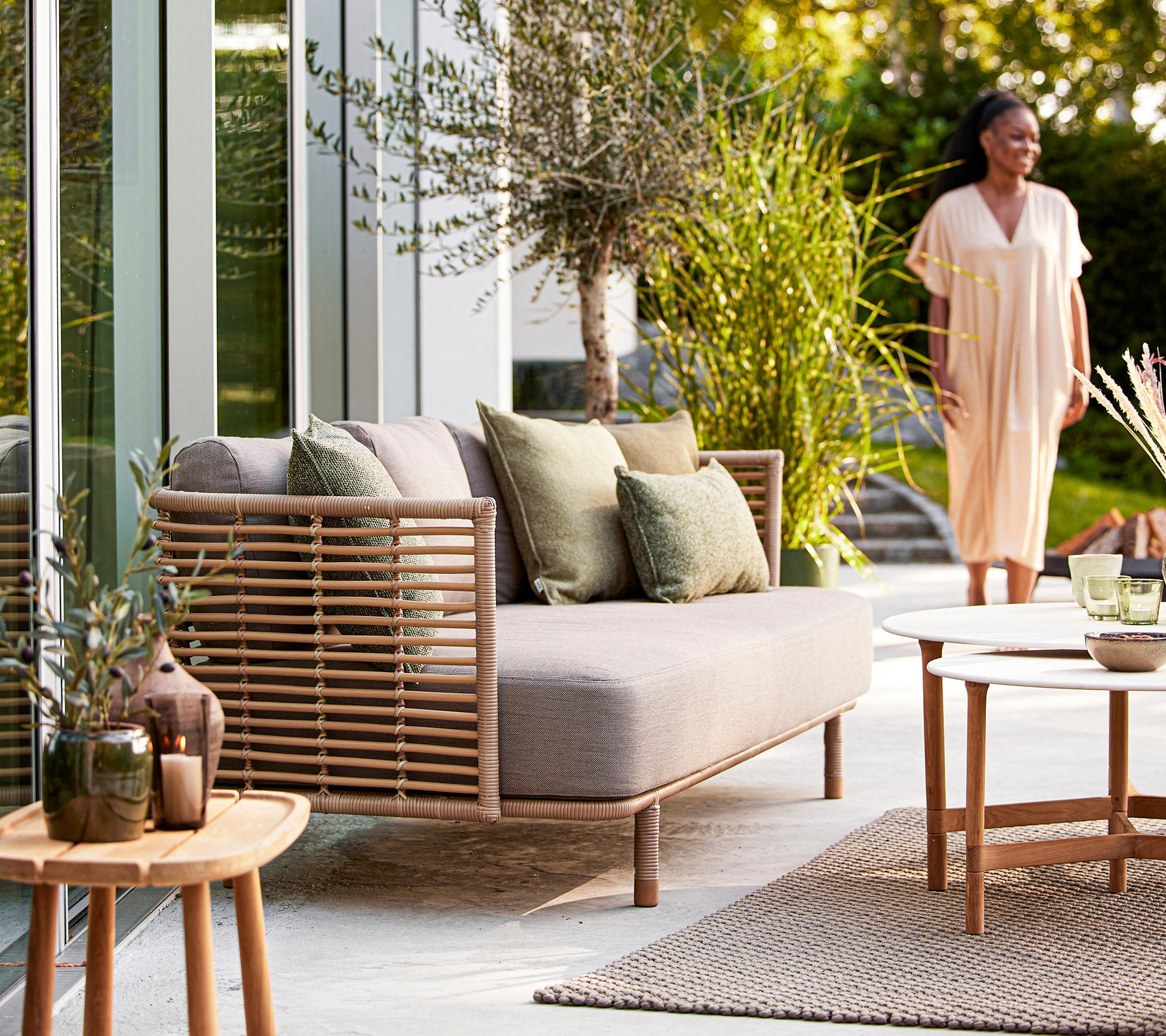 Een gezellige zithoek met een lichte bank, groene kussens, decoratieve planten en een houten tafel, die een uitnodigende sfeer creëert.
