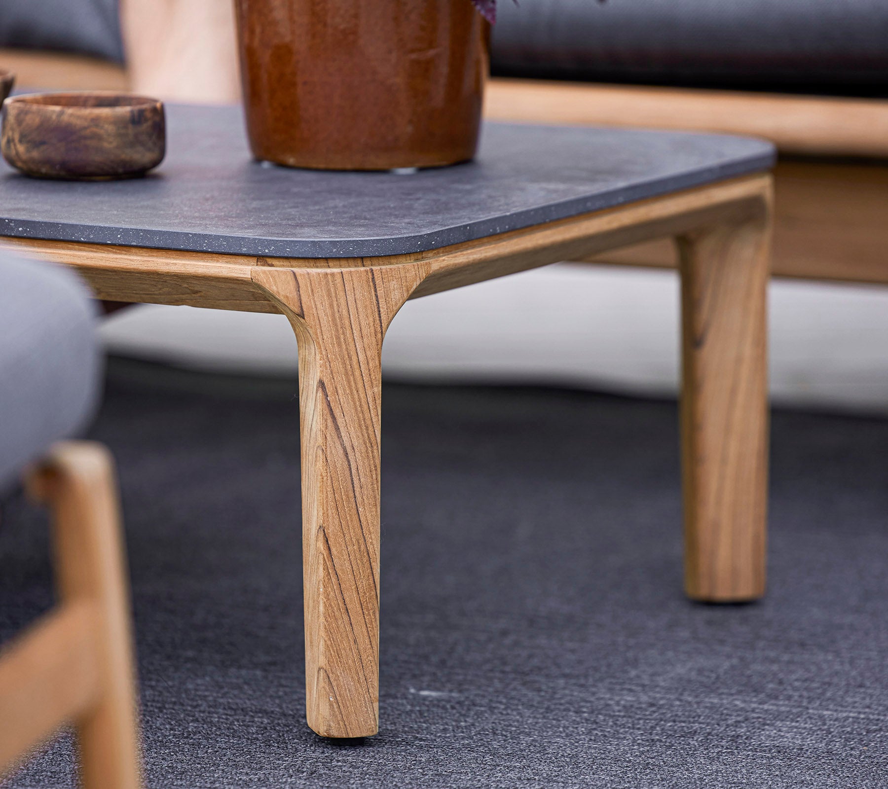 Een houten tafel met een donker stenen blad, voorzien van uniek gebeeldhouwde poten, omringd door zachte zitplaatsen en een decoratieve plantenpot.