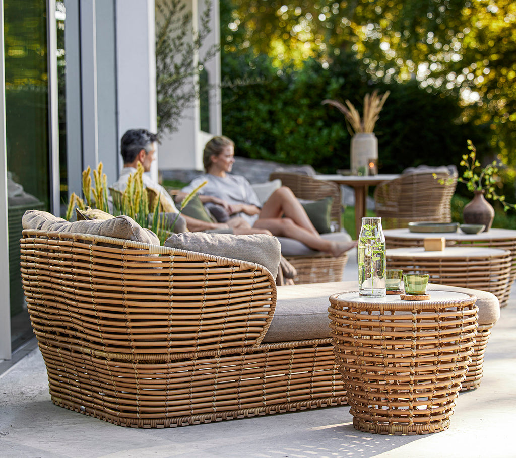 Stijlvolle geweven meubelset met een gezellige zithoek en tafels, aangevuld met decoratieve planten en een ontspannen sfeer.