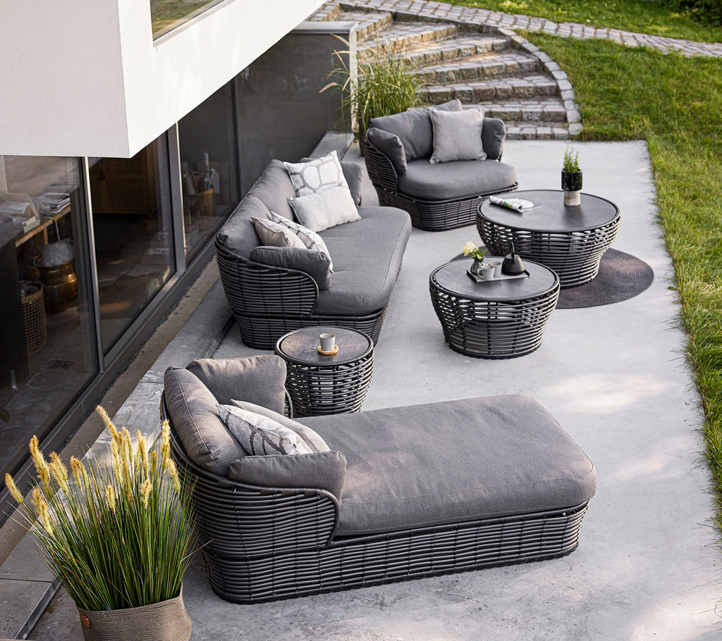 Stijlvolle buitenzitarrangement met een grijze sectie, fauteuils en tafels, aangevuld met decoratieve kussens en planten.