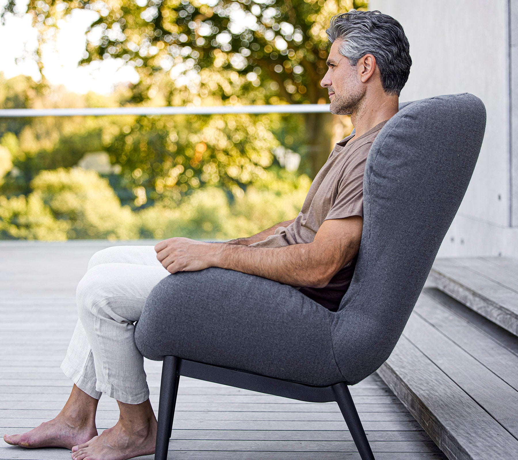 Man die comfortabel zit in een moderne stoel met een slank design, dat zachte bekleding en een elegante, minimalistische vorm laat zien.