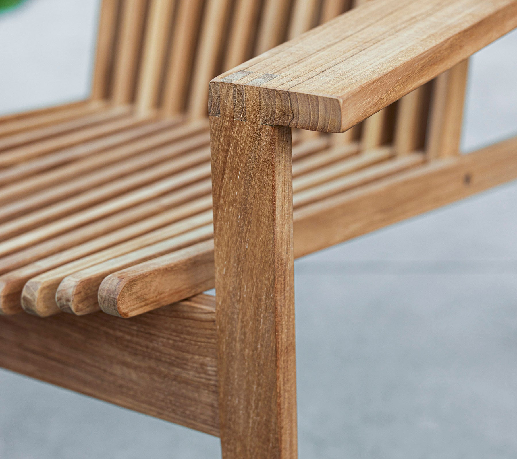 Close-up van een houten bank met een louvredesign en een stevig armleuning, die de natuurlijke houtnerf en ambacht laat zien.