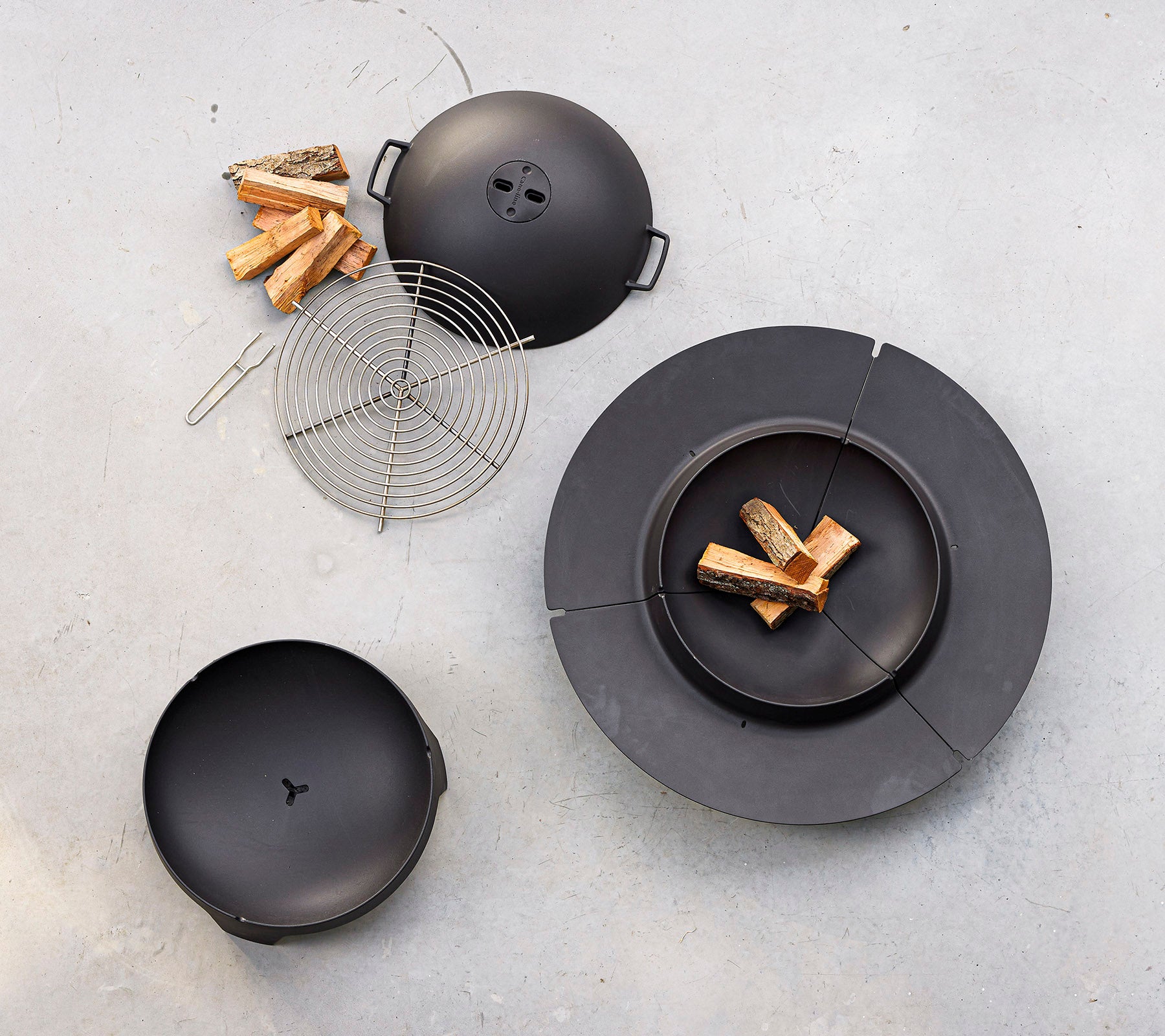 Een zwart kookset met een ronde grill met deksel, een grillrooster en stukken hout in de buurt.