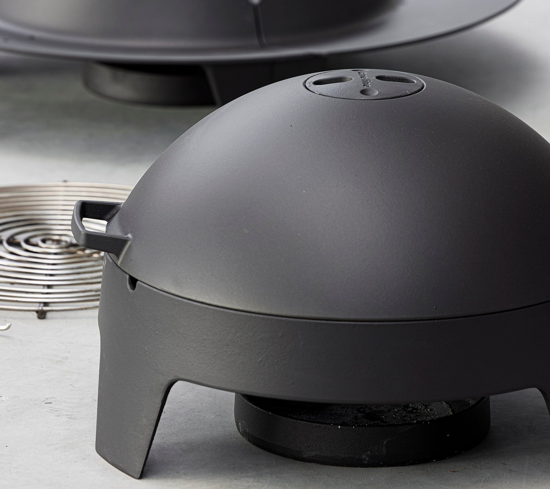 Mat zwarte kooktoestel met een koepelvormig deksel en een verwijderbare warmtebron, ontworpen voor buiten grillen en barbecueën.