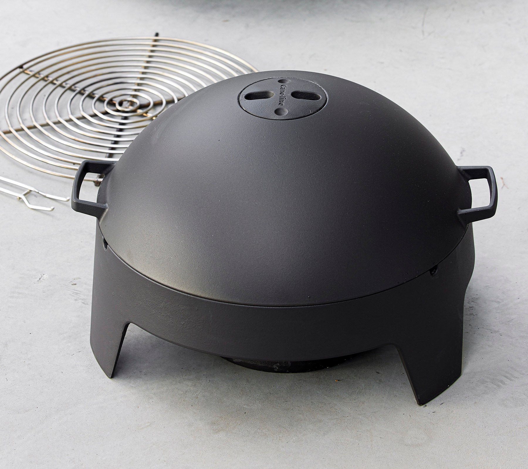 Een slank zwart kookapparaat met een koepelvorm en handgrepen, vergezeld van een cirkelvormig grillrooster. Ideaal voor grillen en koken buitenshuis.