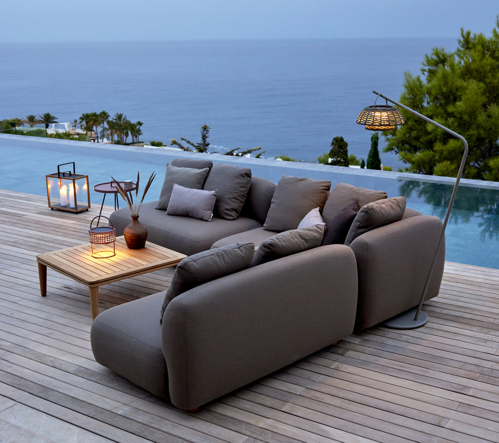 Grijze sofa met houten tafel en lantaarns bij een zwembad met uitzicht op de oceaan.