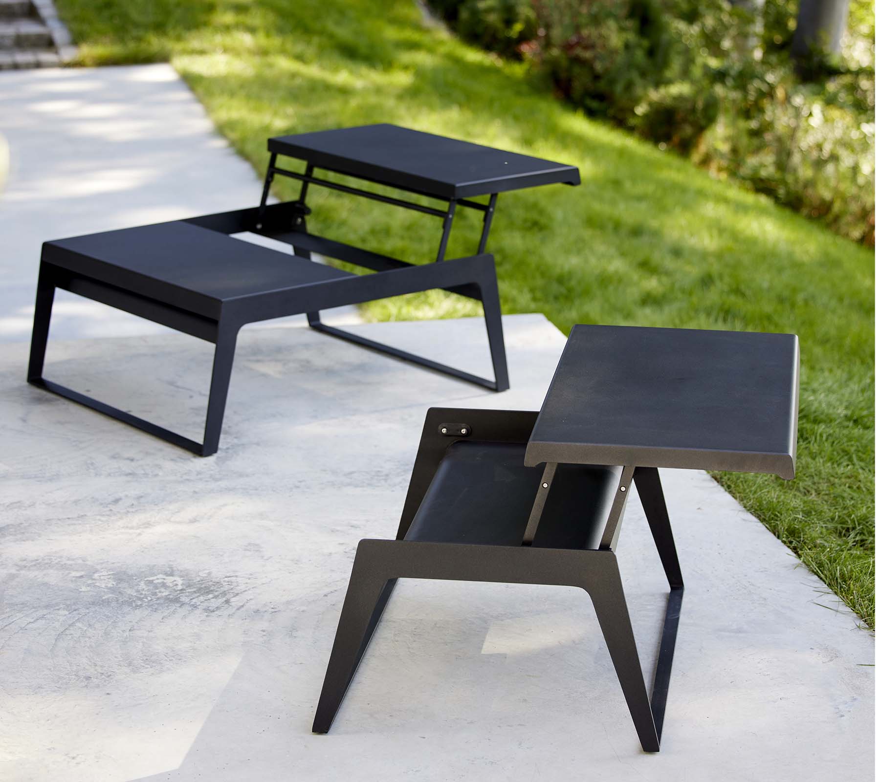 Twee moderne chill-out salontafels met slanke ontwerpen en minimalistische zwarte afwerkingen, die veelzijdigheid in stijl en functionaliteit tonen.