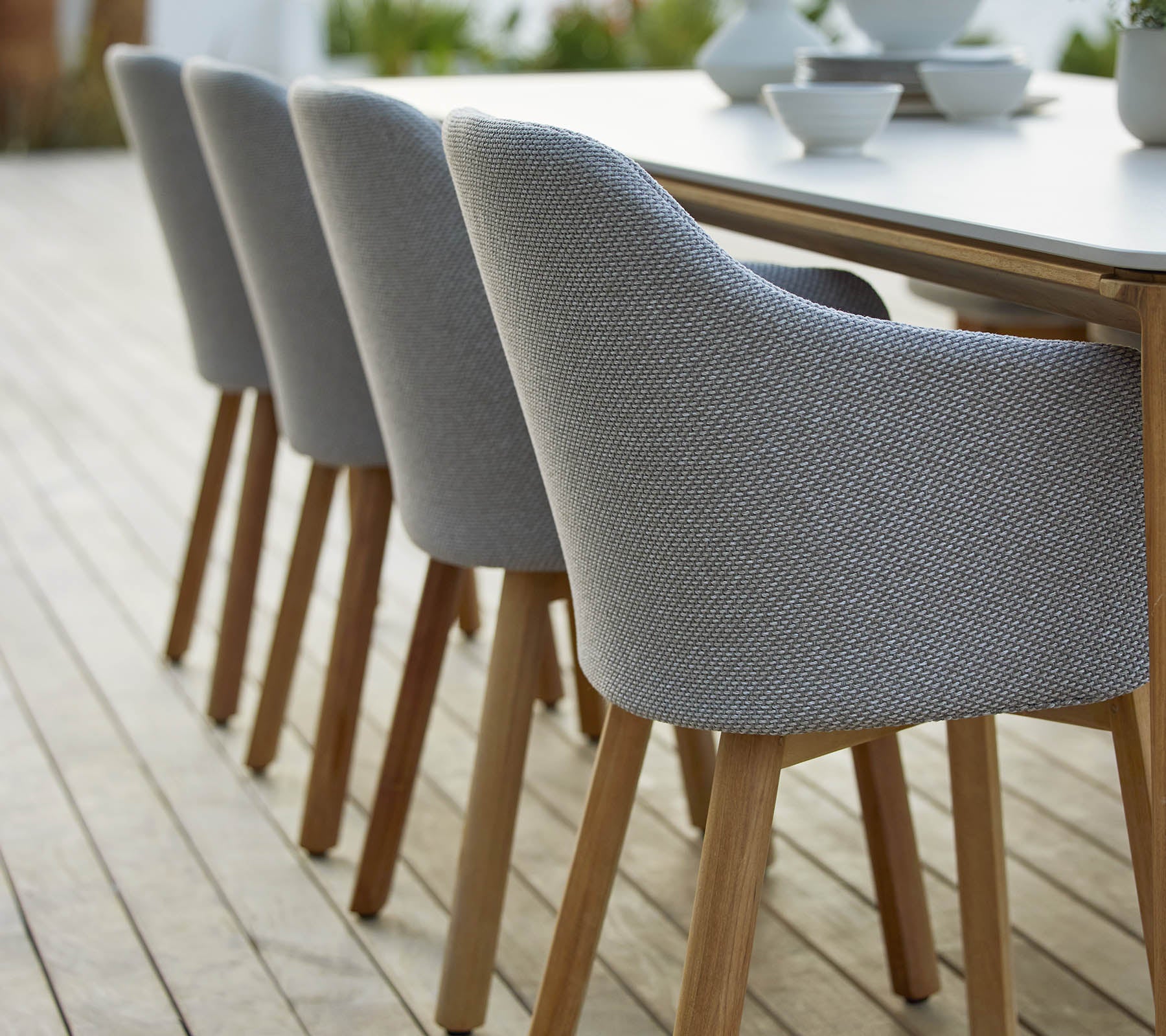 Een rij moderne gestoffeerde stoelen met houten poten, netjes naast een tafel geplaatst, die een stijlvolle en eigentijdse uitstraling laat zien.