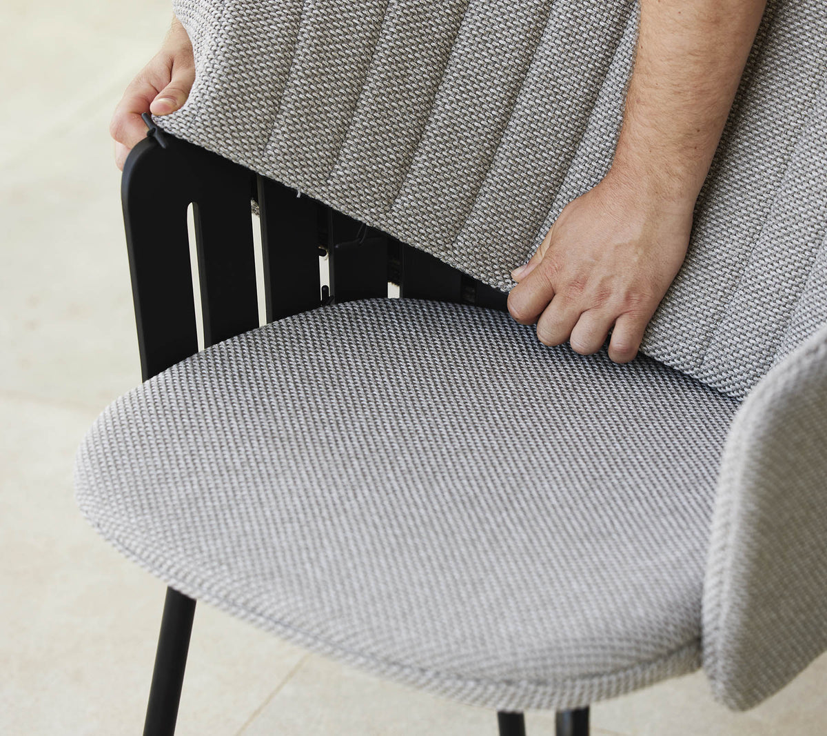 Persoon past de rugleuning van een moderne stoel met een textuurstofzitting aan, die een stijlvol ontwerp en ergonomische ondersteuning toont.
