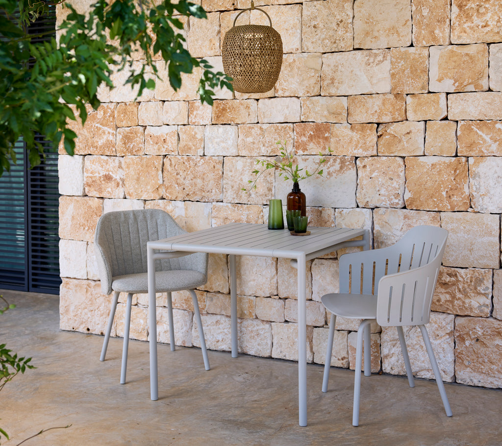 Moderne grijze tafel en stoelen met groene en bruine flessen in een buitenomgeving.