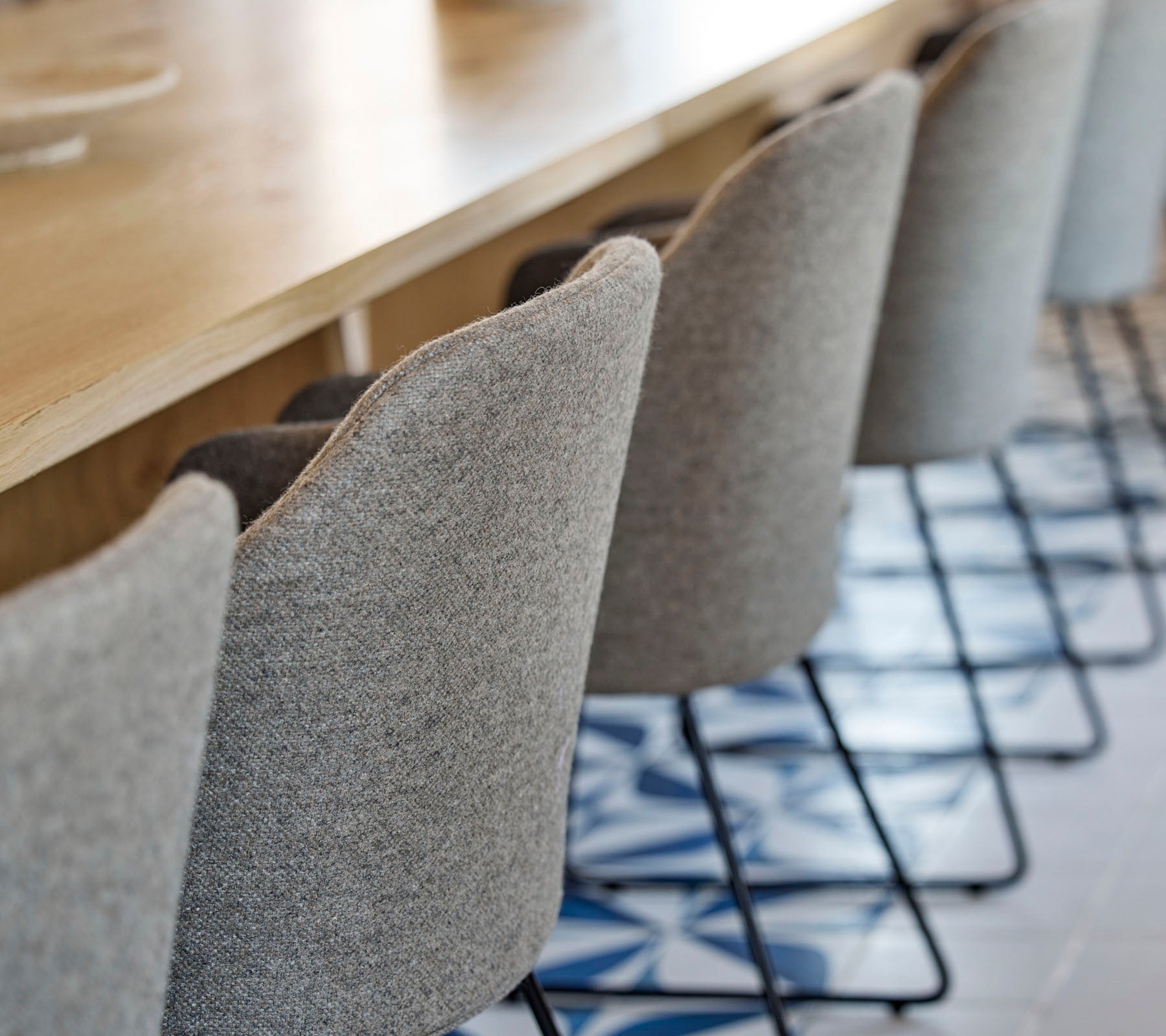 Een rij stijlvolle, gevoerde stoelen met slanke metalen poten rond een houten tafel, met gemustervloer eronder.