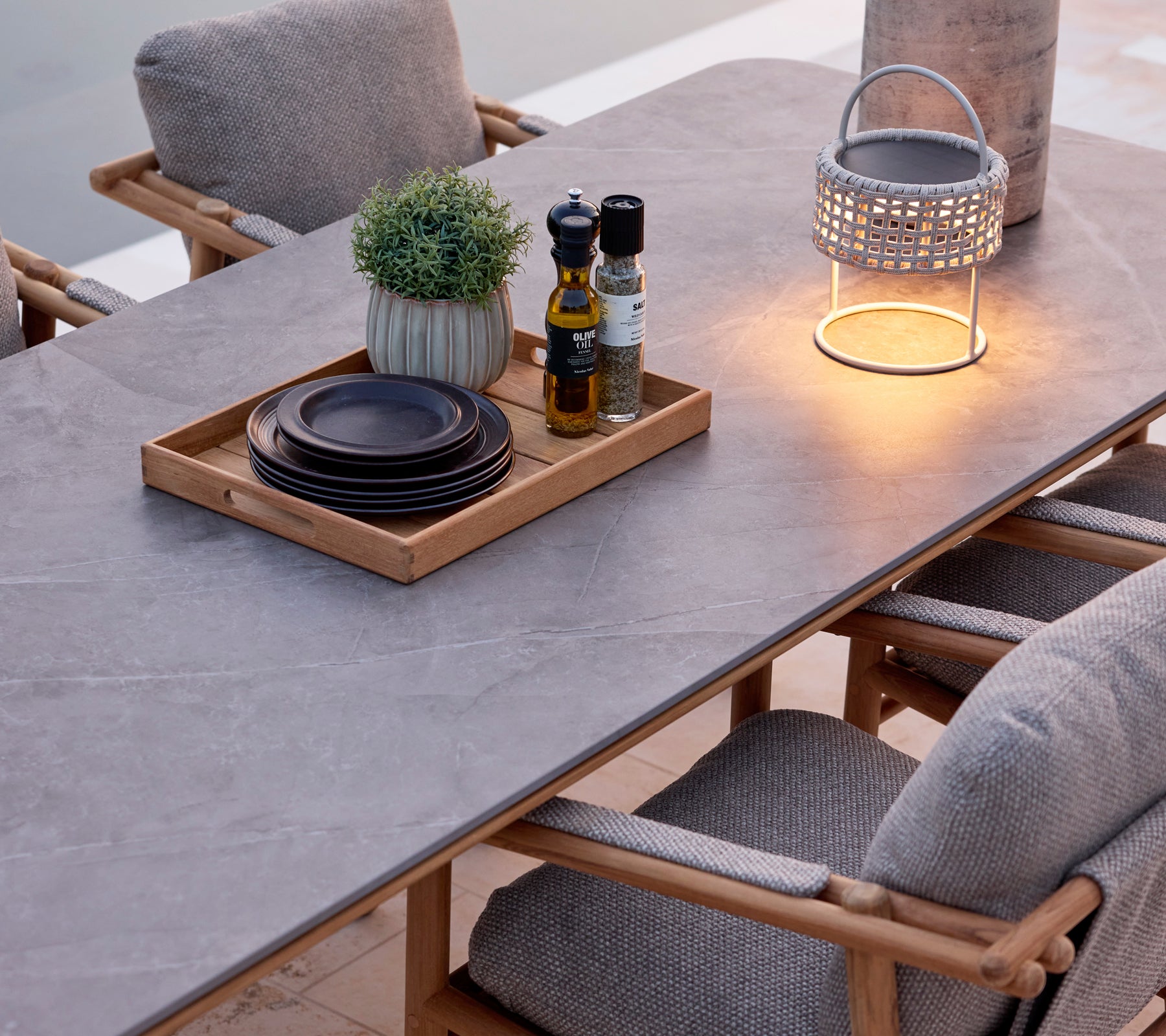 Modern eettafel met grijs oppervlak, bruine stoelen, zwarte borden en een decoratieve lantaarn.