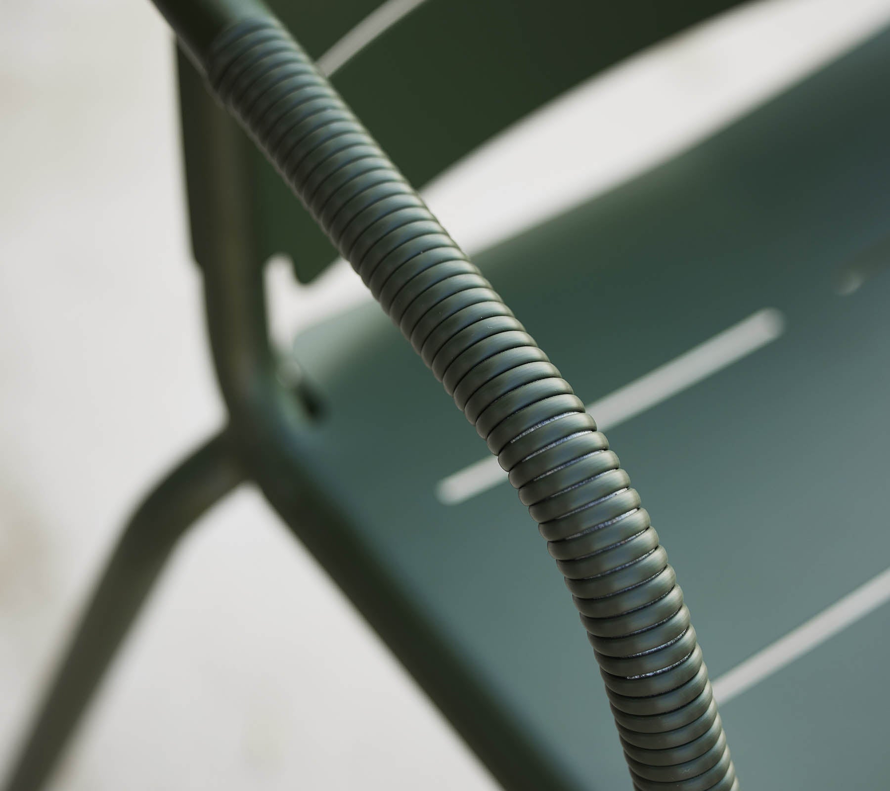 Close-up van een groene Copenhagen stoel, waarbij de gebogen armleuning en het slanke ontwerp met subtiele sleuven in de zitting worden benadrukt.