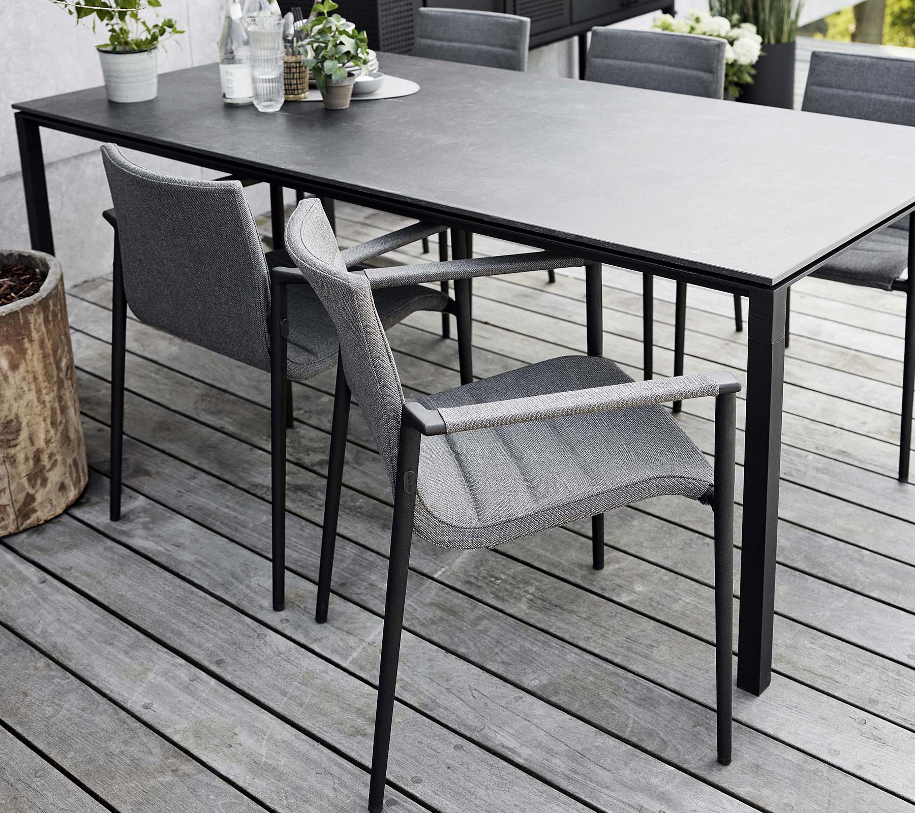 Stijlvolle eetopstelling met een strak tafeldesign en moderne grijze kernstoelen, omringd door natuurlijke elementen en groen.