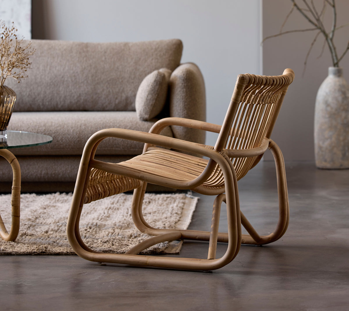 Rattanstoel naast een beige bank en een glazen tafel in een moderne lounge-instelling.