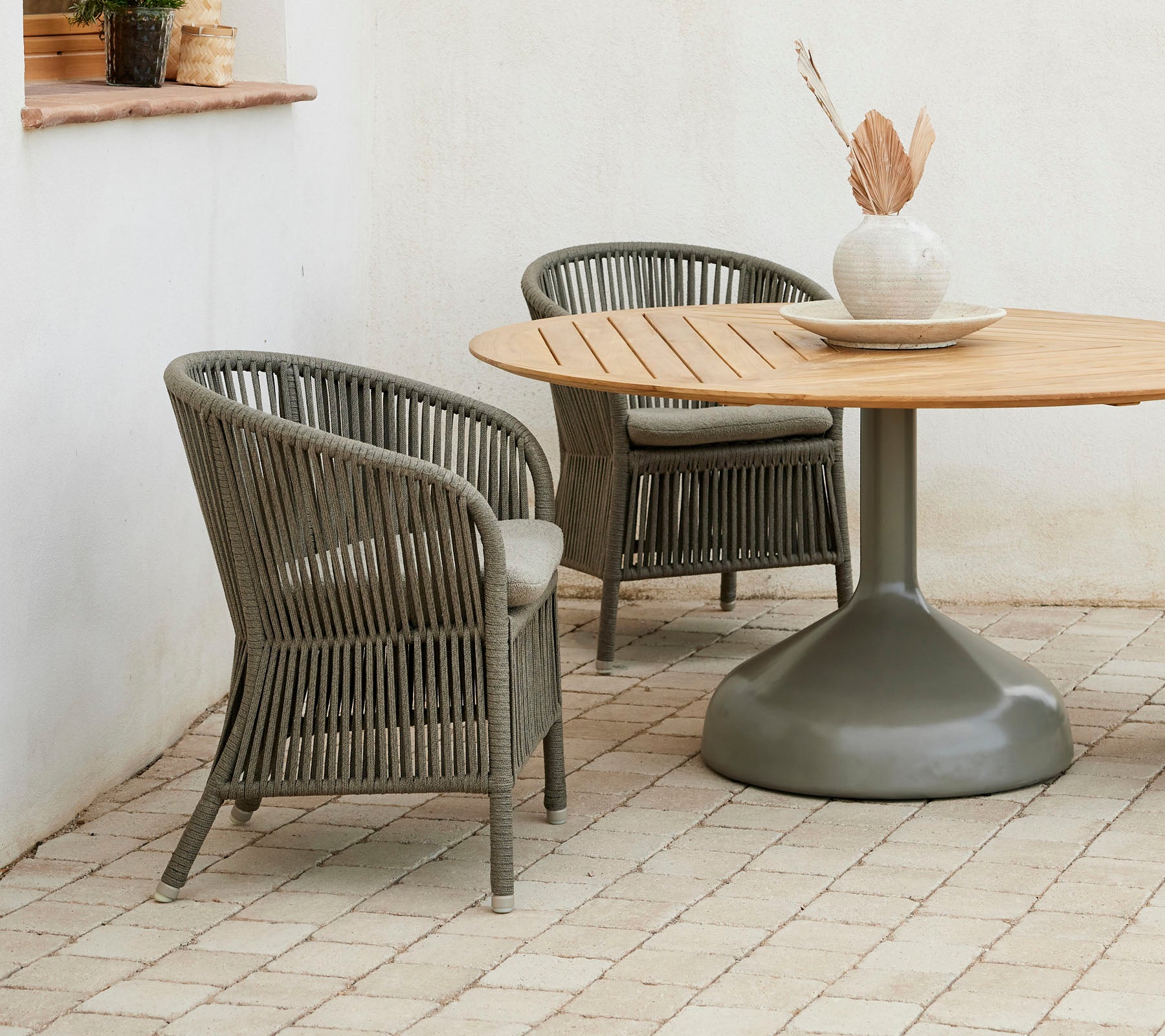 Twee stijlvolle Derby-stoelen in combinatie met een ronde Glaze-eettafel, met een neutraal kleurenpalet en een decoratieve vaas.