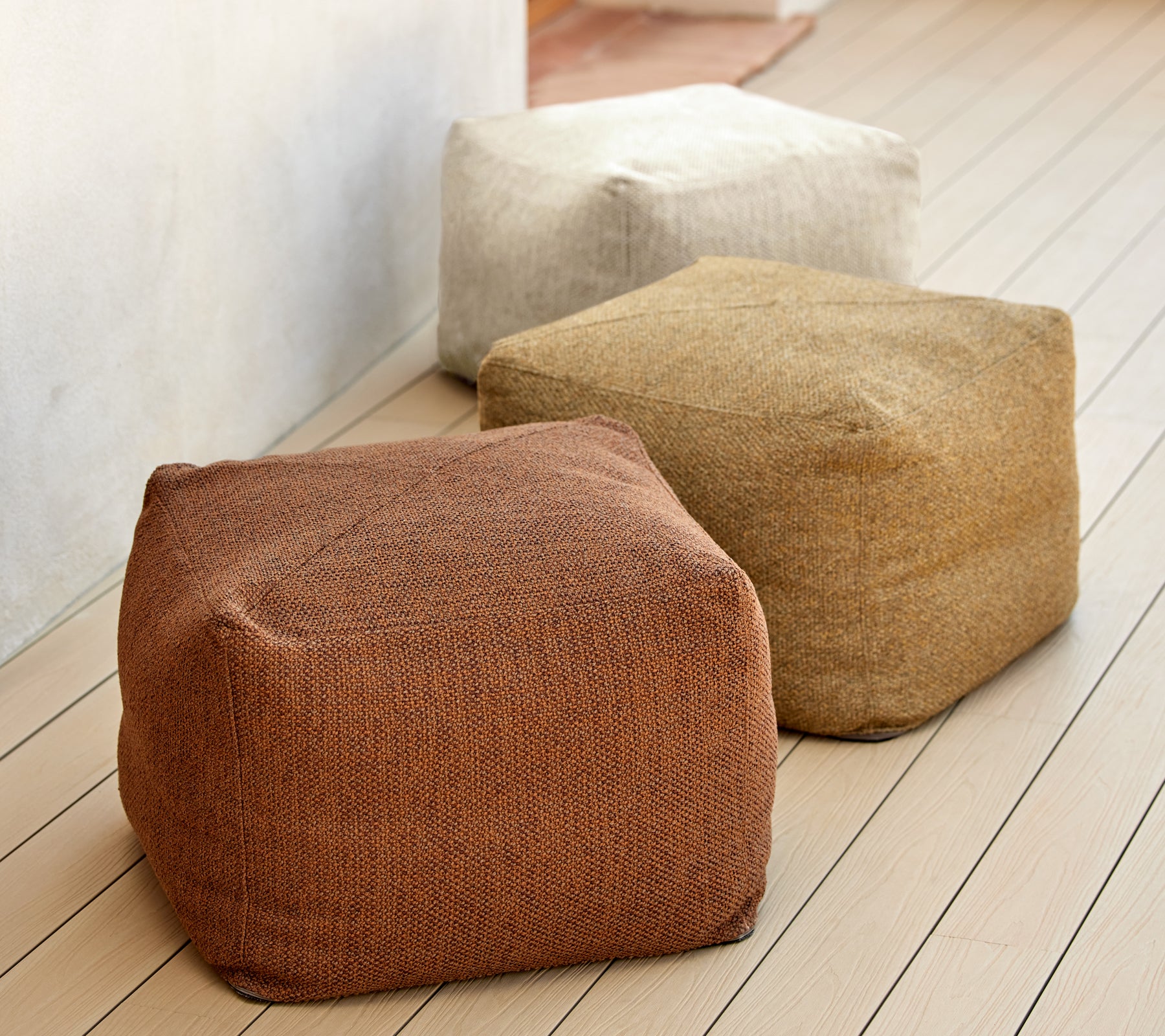 Drie gestructureerde poefs in aardetinten van bruin, beige en tan, weergegeven op een houten oppervlak. Ideaal voor veelzijdige zitplaatsen en decor.