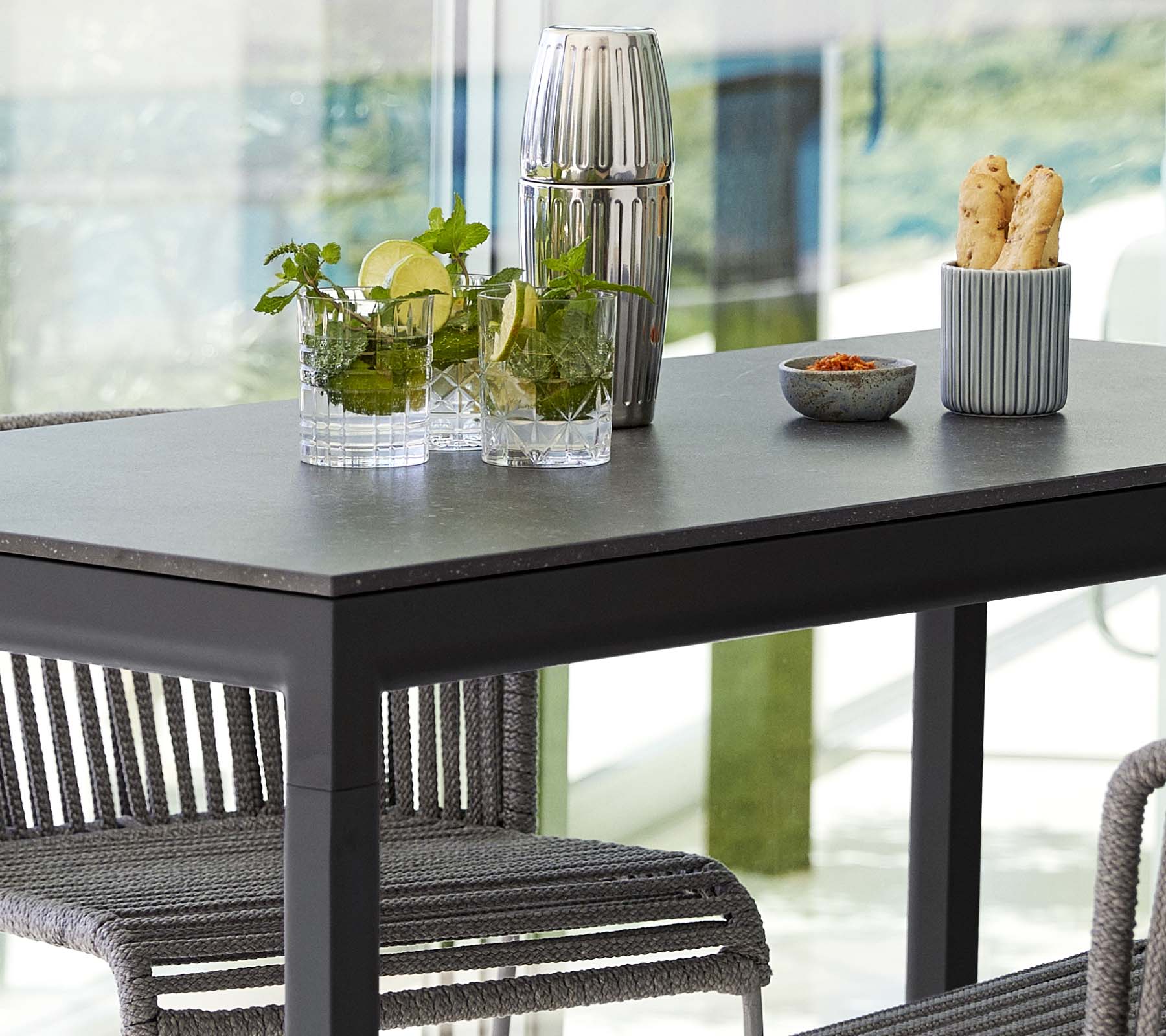 Een moderne tafel gezet met planten in glazen vazen, een decoratieve container en een schaal met snacks, omringd door stijlvolle stoelen.