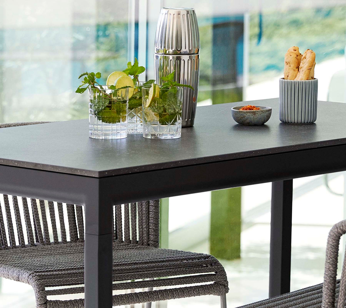 Een moderne tafel gezet met planten in glazen vazen, een decoratieve container en een schaal met snacks, omringd door stijlvolle stoelen.