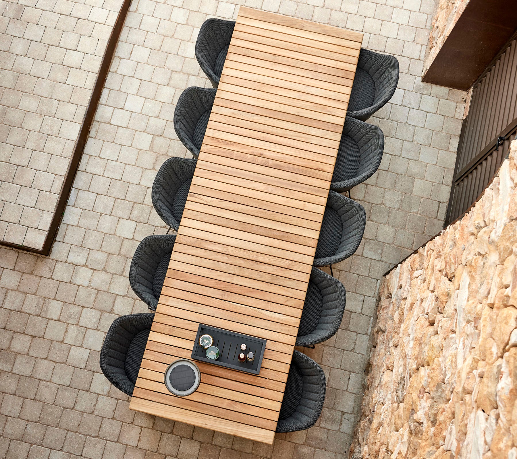 Een lange houten tafel met gespleten ontwerp, omringd door ronde zwarte stoelen, met een klein dienblad met kopjes bovenop.