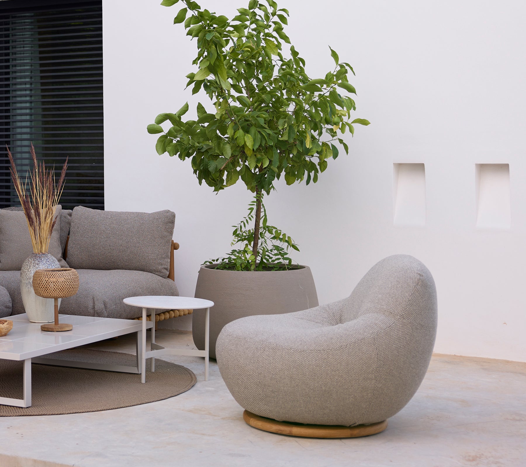 Moderne loungegebied met een grijze stoel, bank, witte salontafel en groene plant.
