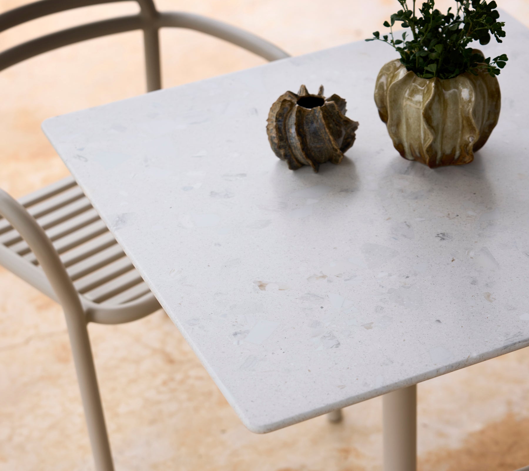 Witte tafel met een grijze stoel en een groen plantenhighlight.