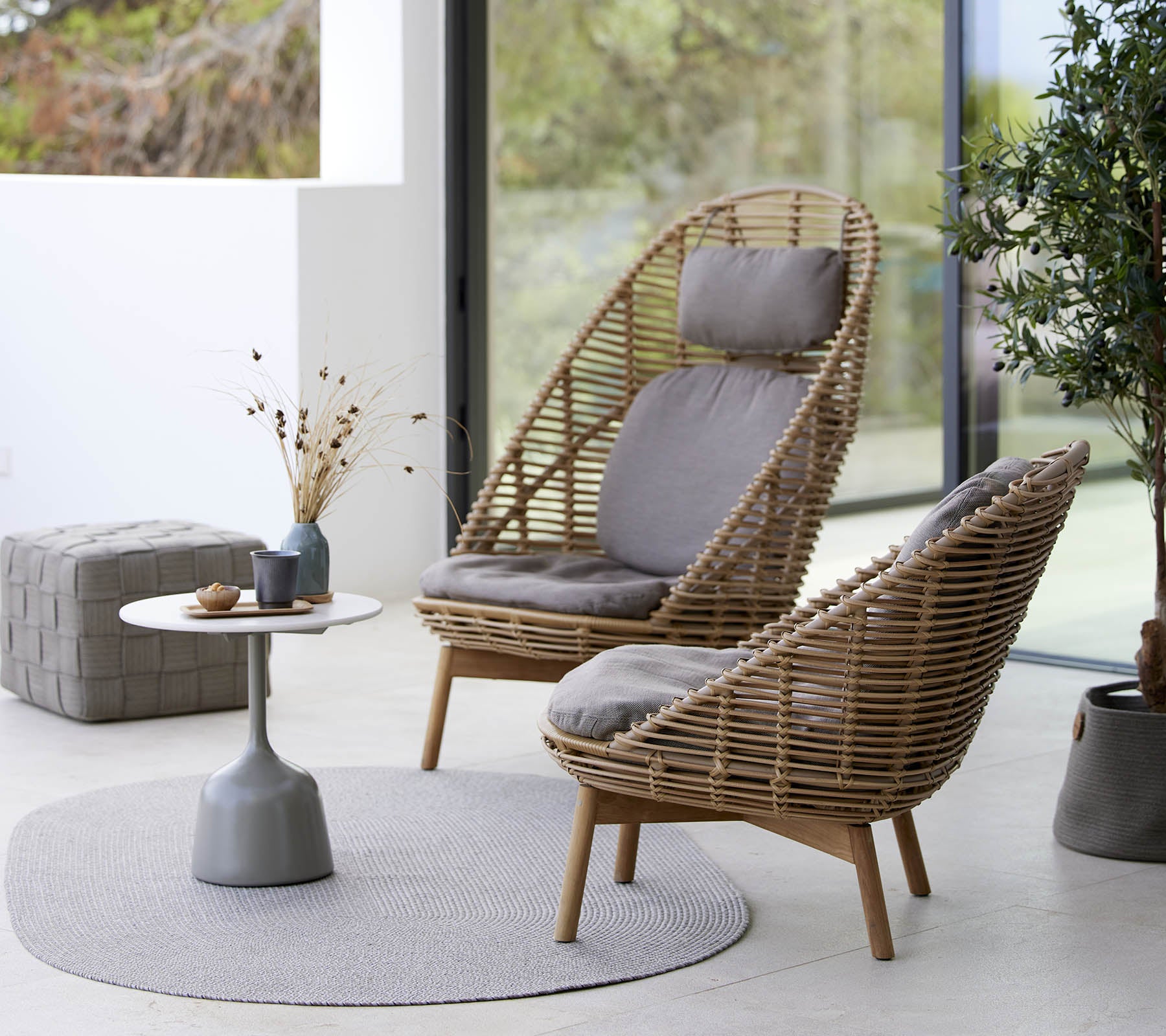 Twee stijlvolle geweven stoelen met kussens, vergezeld van een klein rond tafeltje en decoratieve elementen, geplaatst op een rond tapijt.