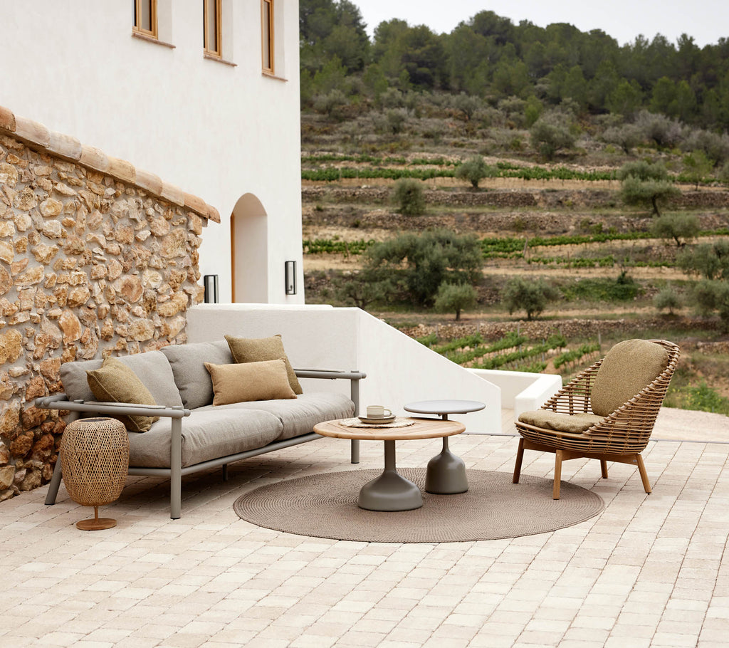 Een Hive loungechair en Sticks-sofa, gerangschikt met een ronde tafel en decoratieve elementen, tegen een sereen landschap.
