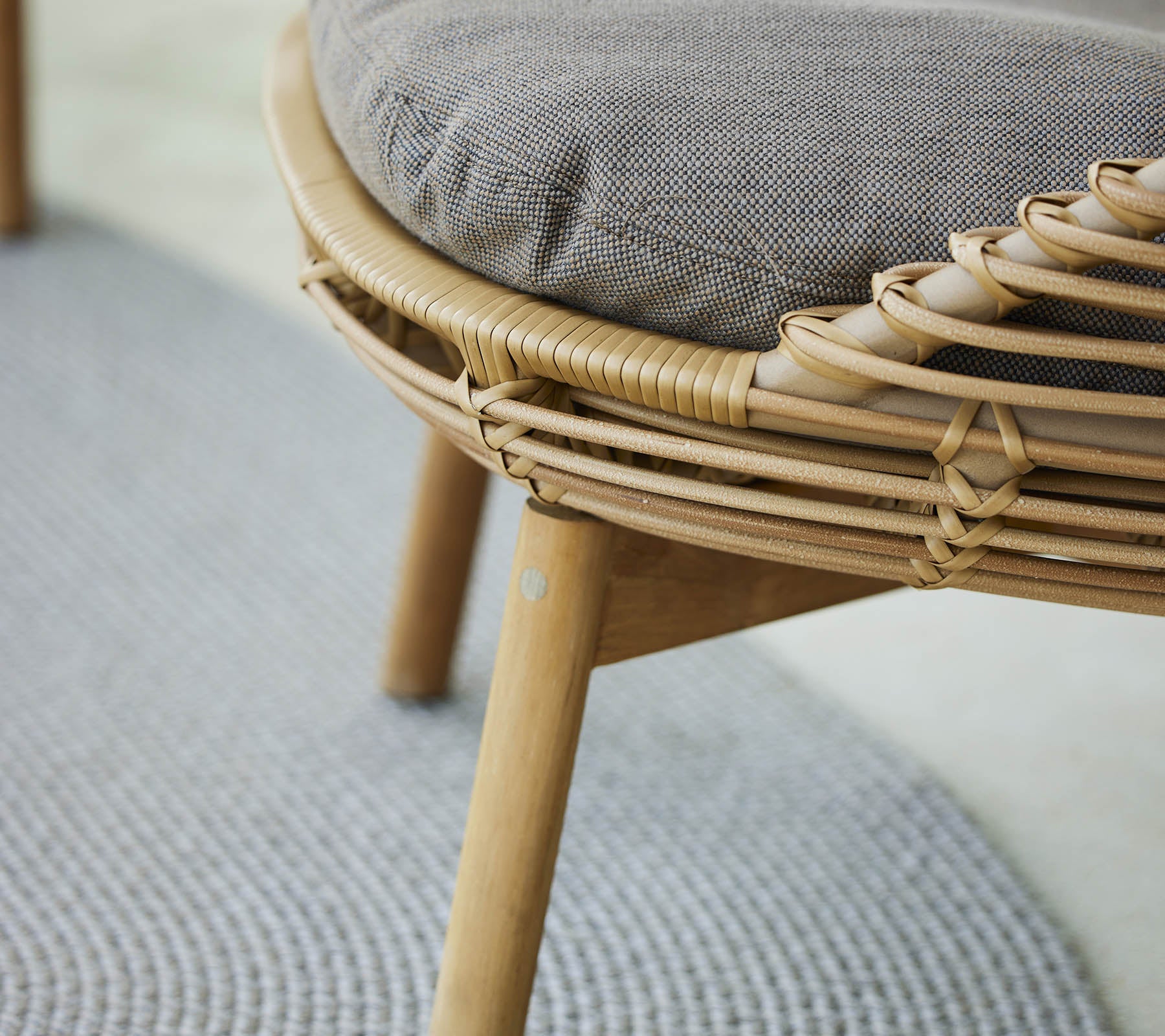 Een close-up van een stijlvolle loungestoel met een geweven frame en een gevoerd zitvlak, aangevuld met een gestructureerd vloerkleed eronder.
