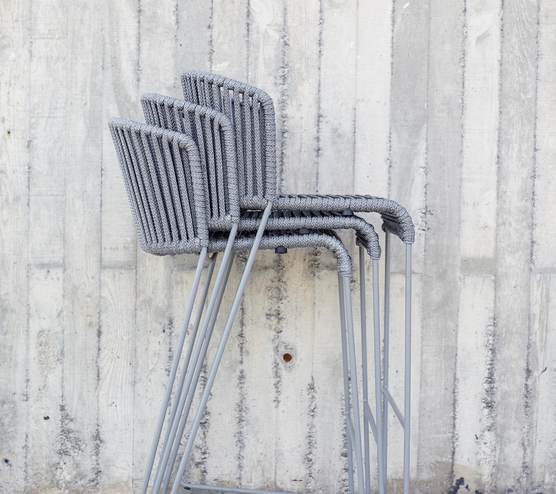 Gestapelde grijze stoelen tegen een gestructureerde betonnen muur.
